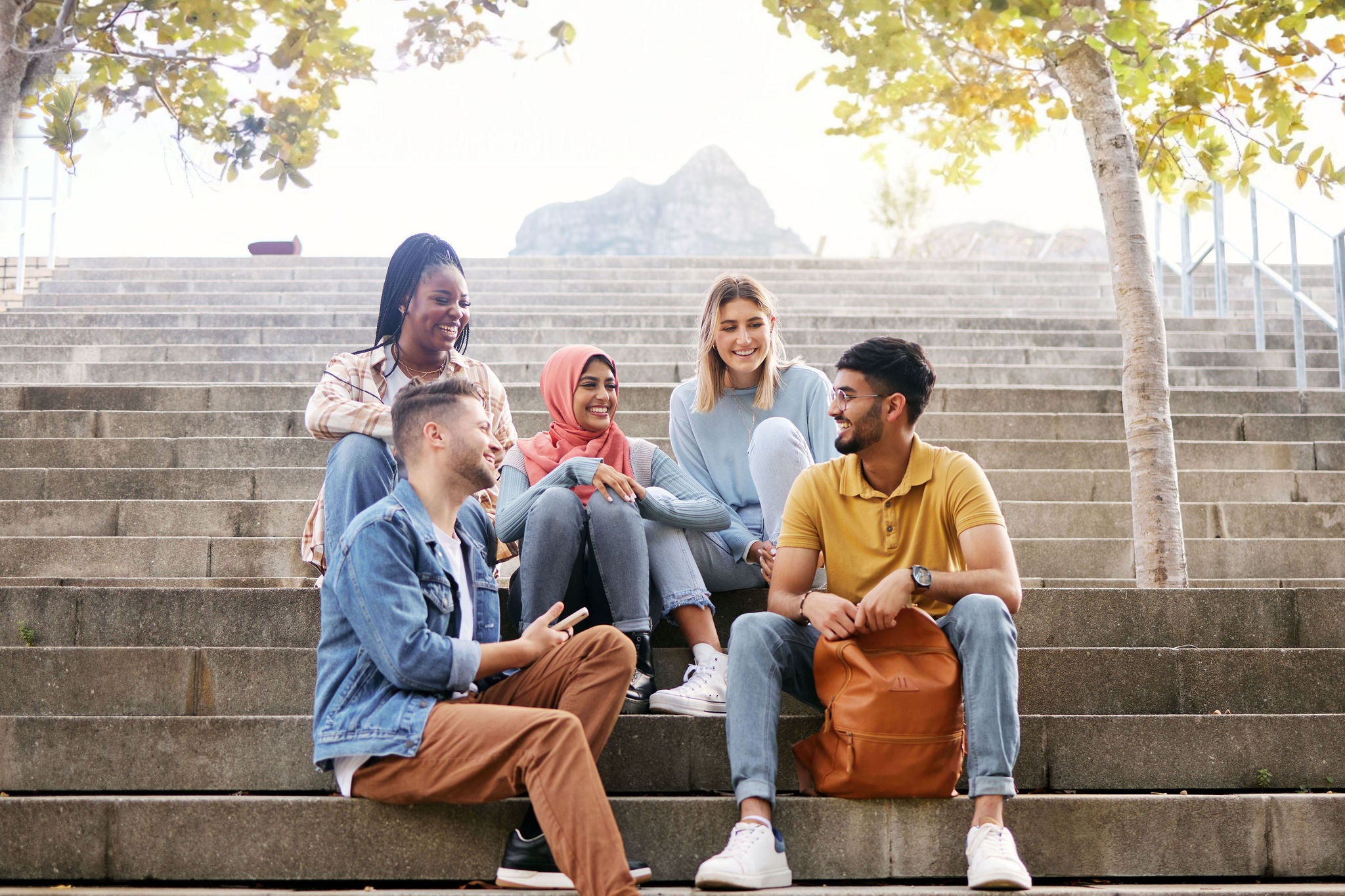 Relax, friends or students on stairs at break talking or speaking of future goals or education on campus. Diversity, school or happy young people in university or college bonding in fun conversation.