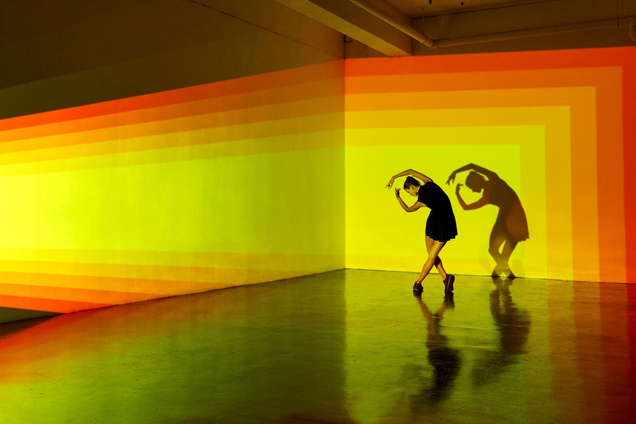 Girl dancing in an abstract space with strong graphic shapes being projected onto the walls behind her