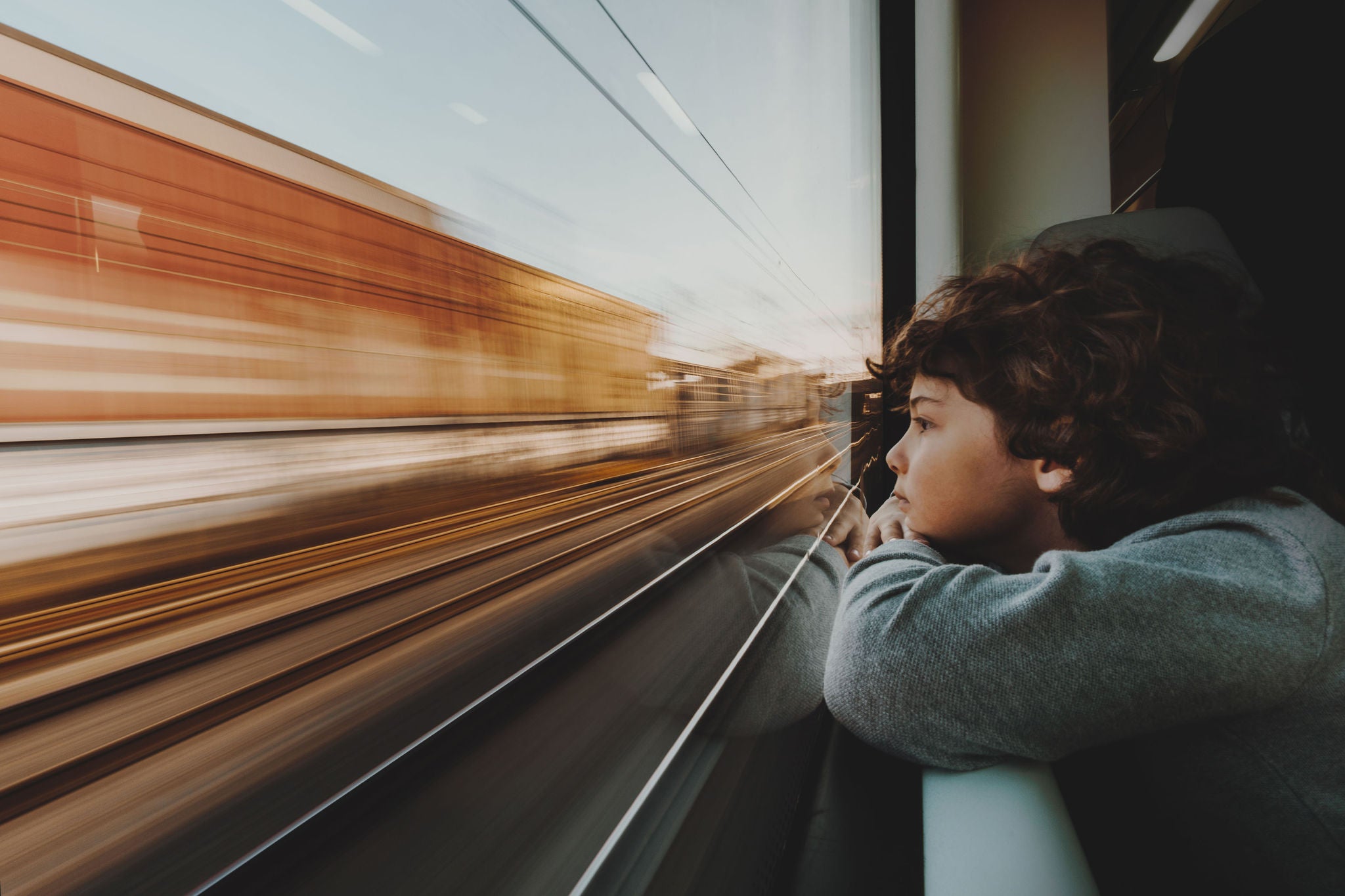 Boy leaning on a window sill looking through a train window