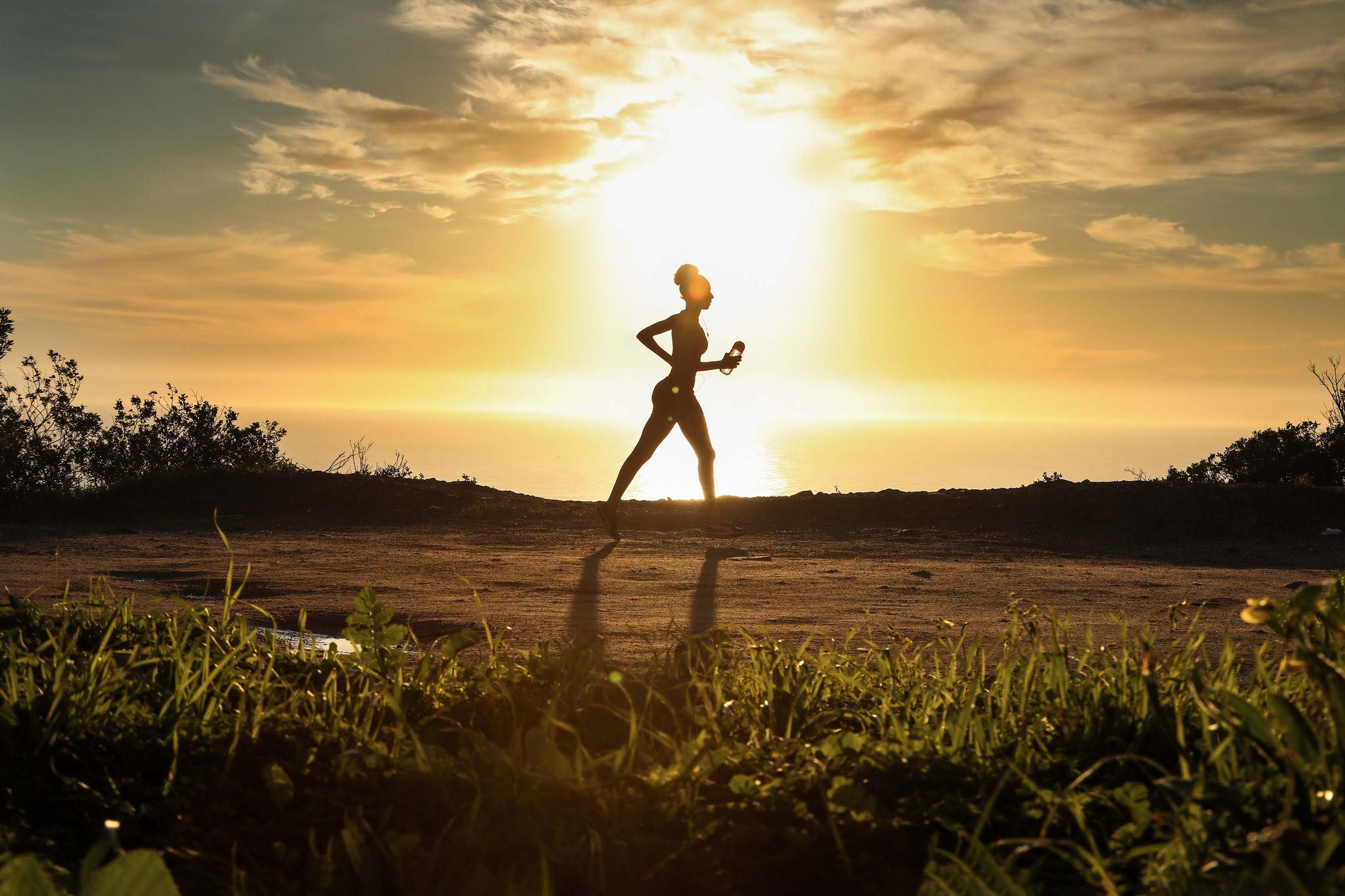 Woman trail running with sun behind her background