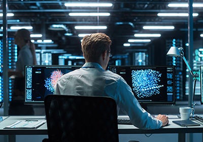In the Futuristic Laboratory or Office Male Scientists Working at the Two Monitors. Developer Writing Code at the Evening. Computer Engineer Create Neural Network at His Workstation
