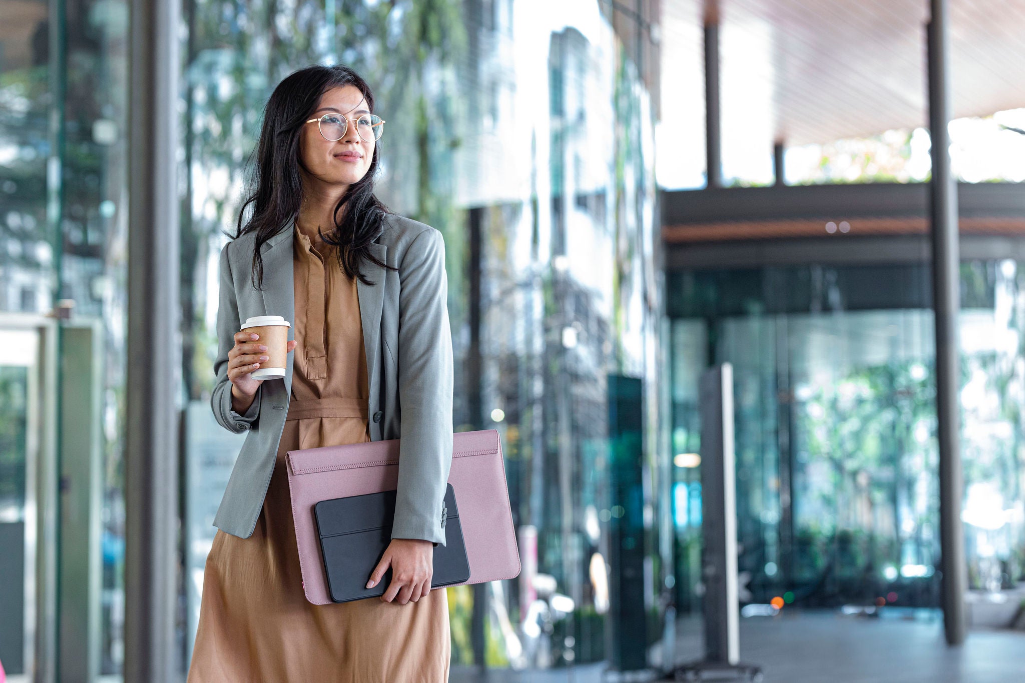 Outdoor shot of a smiling Asian businesswoman holding coffee and files on the street.