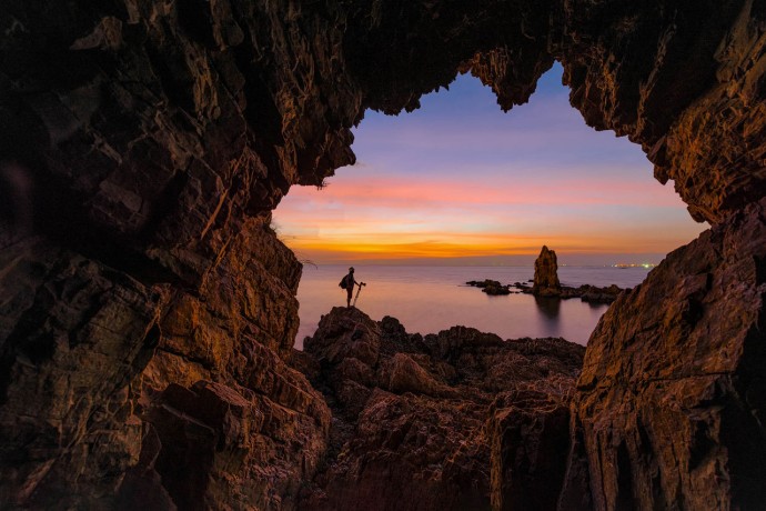 Photographer stands in rock arch at sunset
