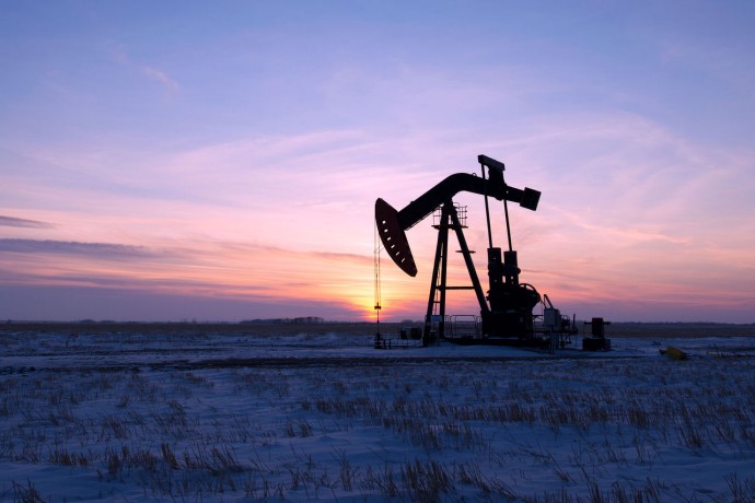 An oil drilling rig and pumpjack on a flat plain in the canadian oil fields at sunset