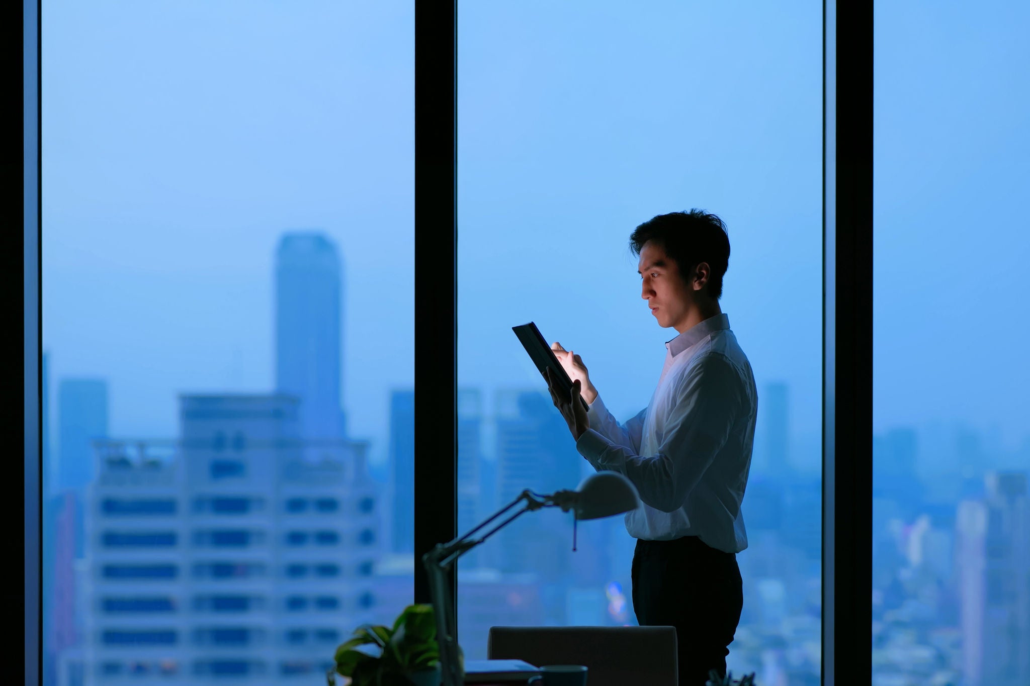 Side view of Asian business man standing in office using tablet at night