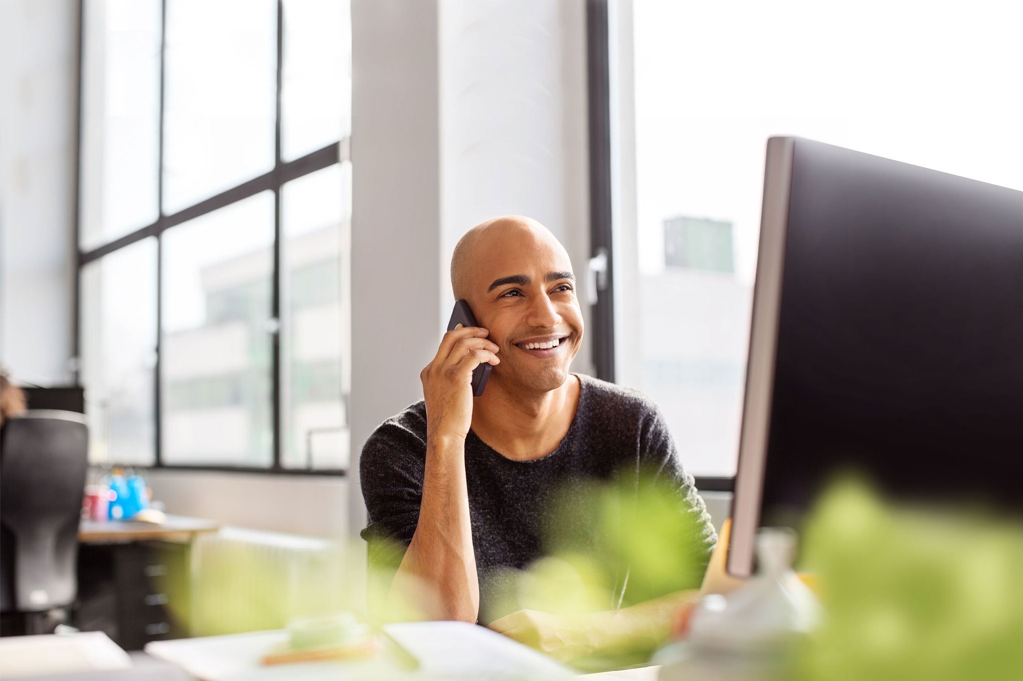 Mature man talking on phone and smiling. Hispanic male professional working at his desk in office.