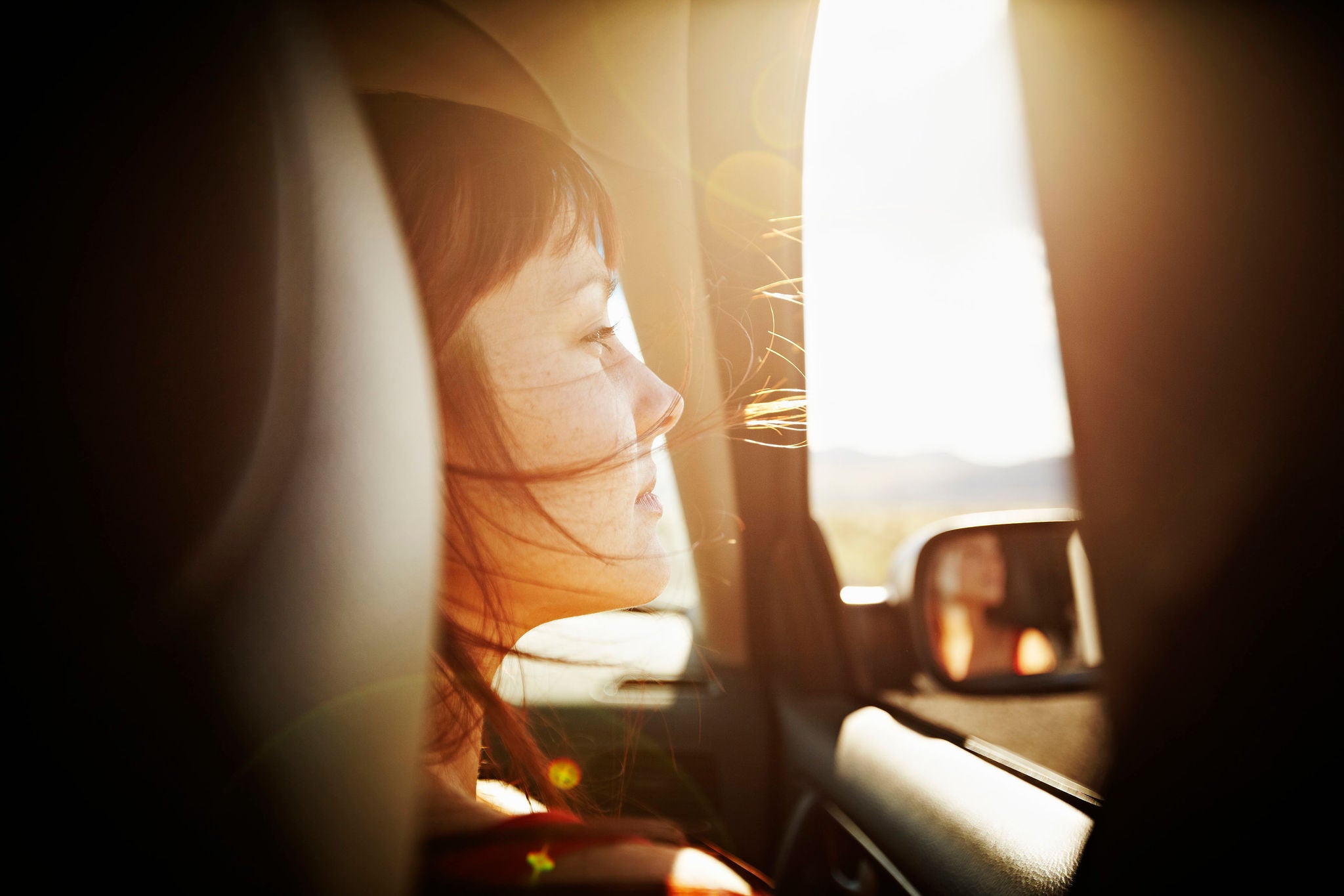 Woman with hair blowing looking out window of car at desert landscape