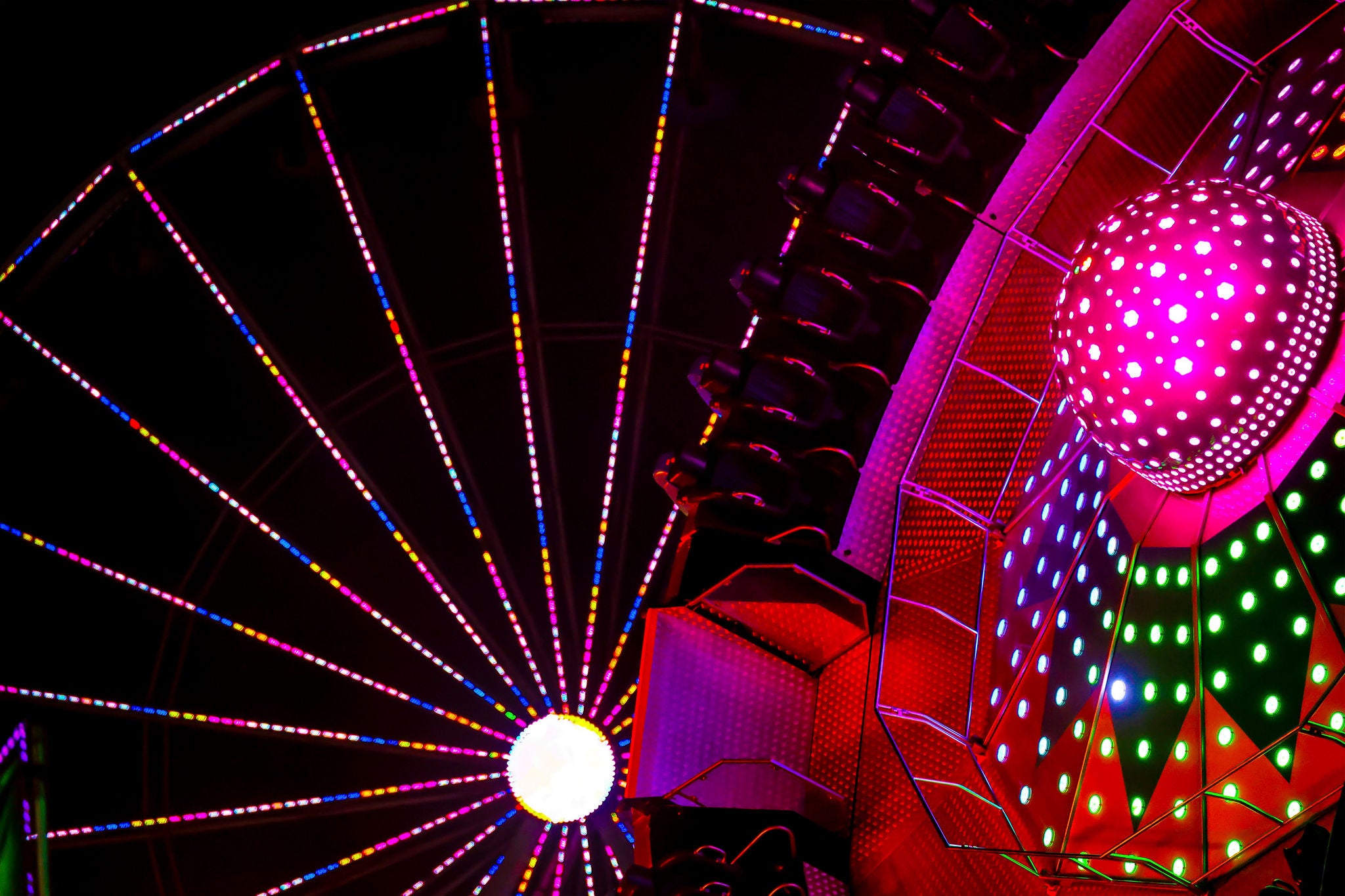 Colorful carnival ride illuminated with vibrant LED lights, featuring a glowing sphere against a dark night sky