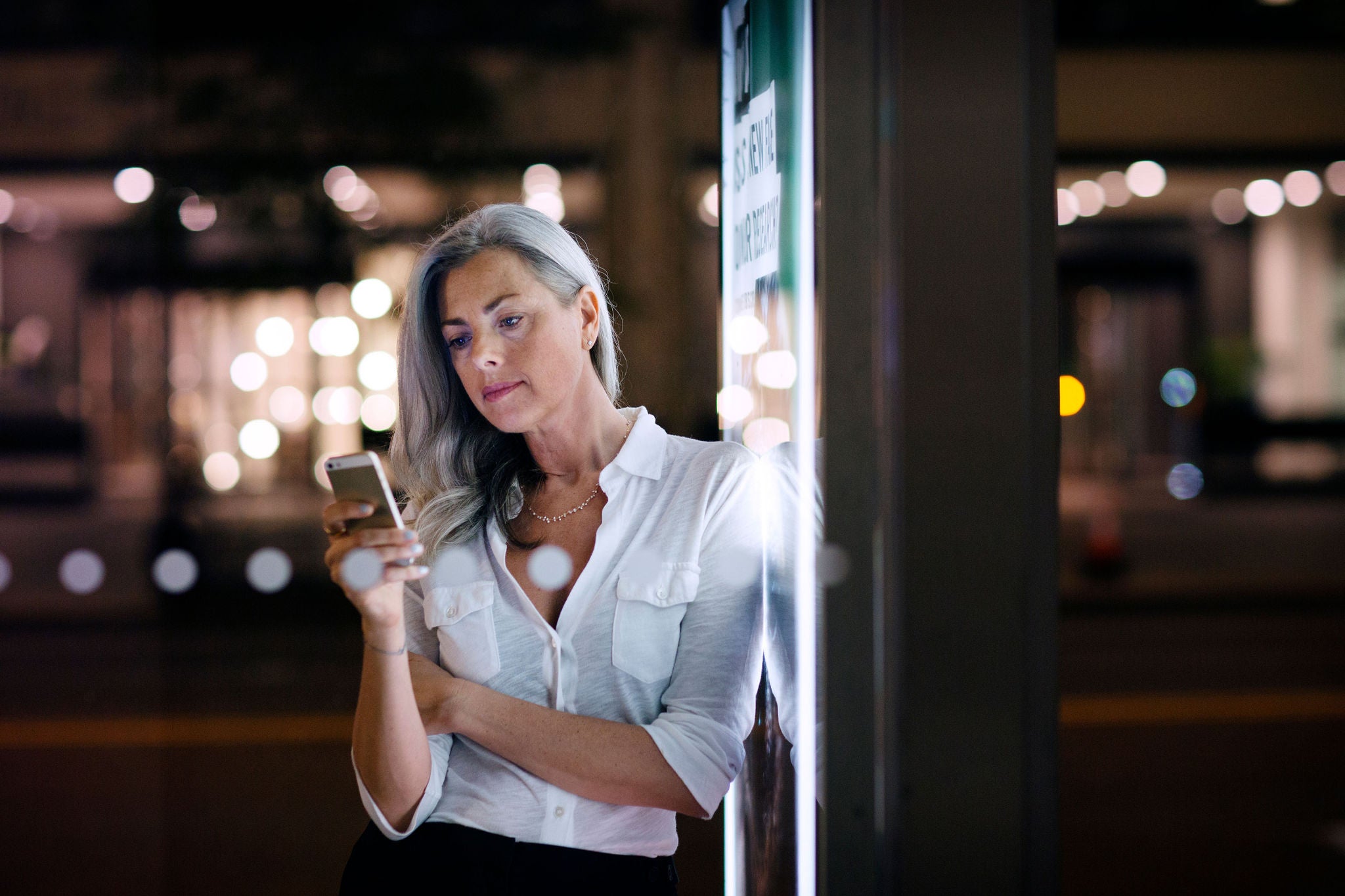 Businesswoman using phone while leaning on bus stop poster in city