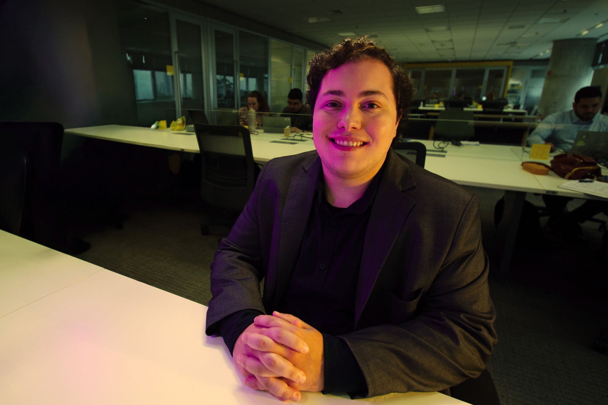 Persona sonríe a cámara sentada en un escritorio en una oficina