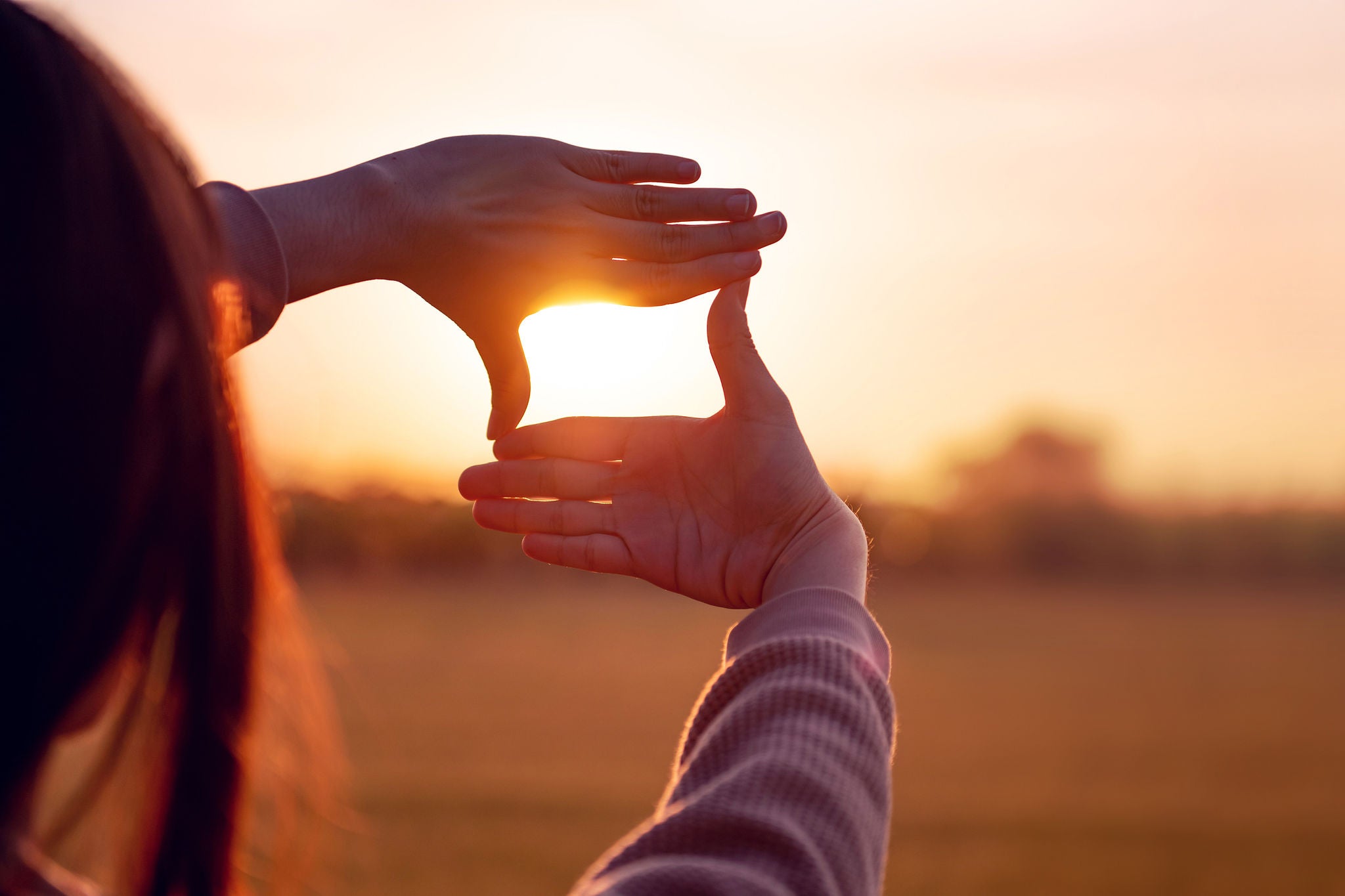 Girl framing sunset with hands