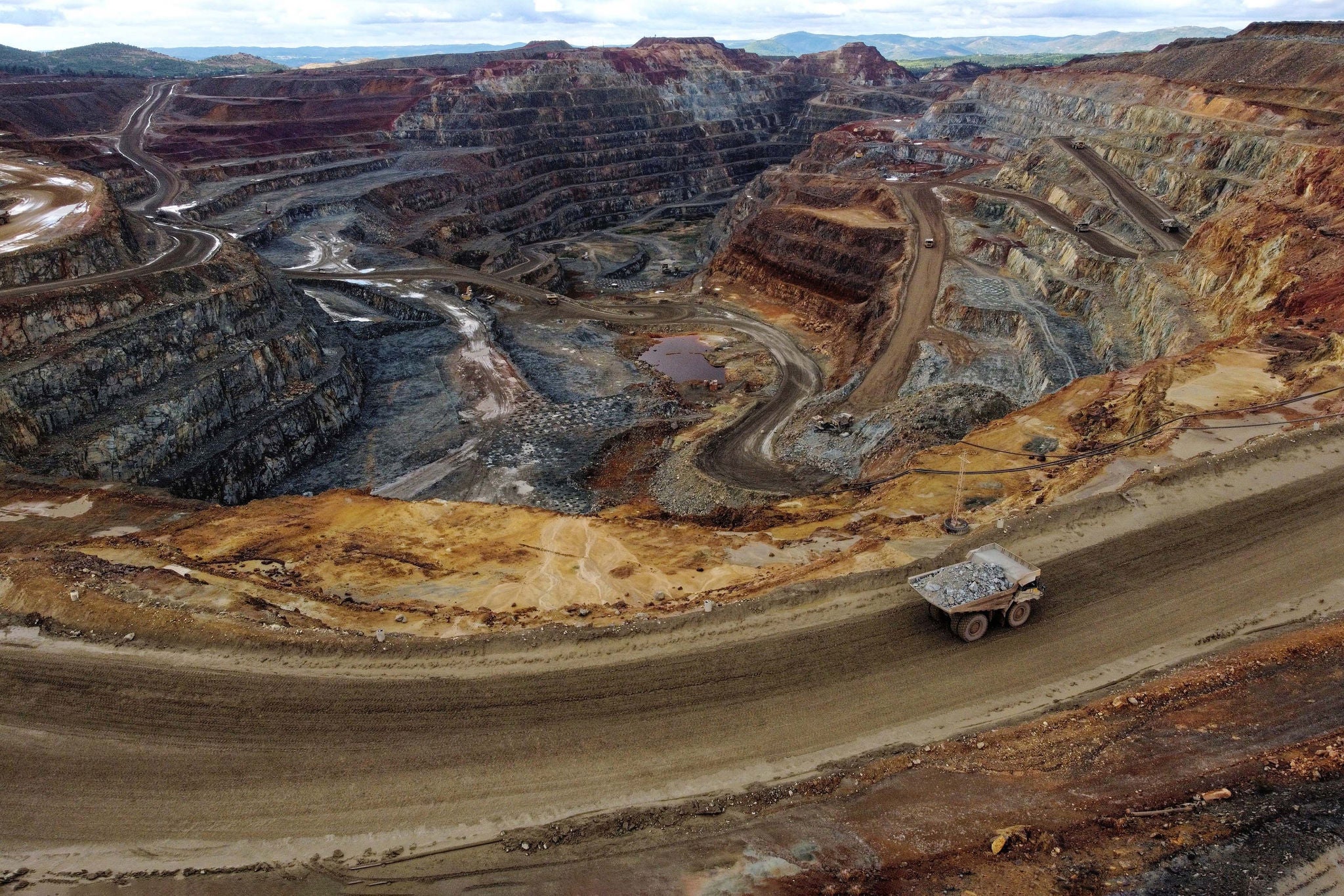 Open pit copper mine in Spain as seen from the viewpoint outside. One loaded dumptruck climbs the hauling road while the pit behind it shows all the red colours from different minerals