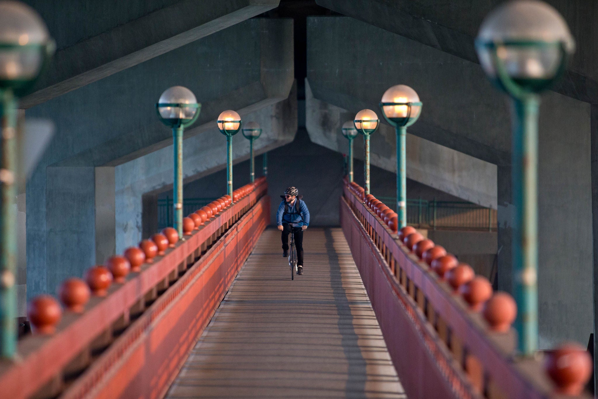 A male bike messenger rides over a bridge on his way to make a delivery. He is riding a fixed gear or one speed bicycle.
