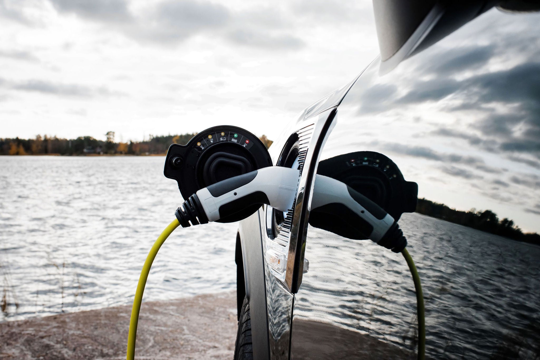 Voiture électrique en charge au bord d’un lac sous ciel nuageux