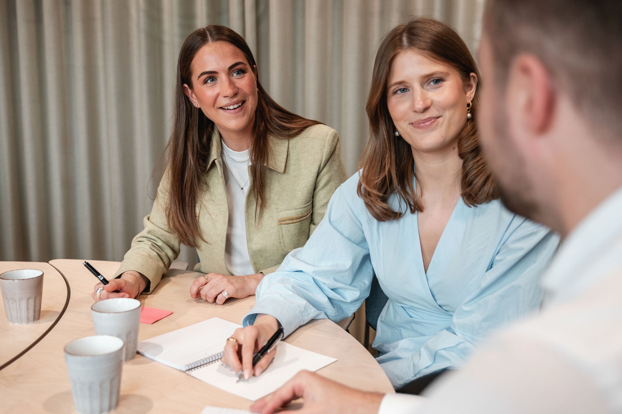 Tre kollegor sitter runt ett bord i ett mötesrum och antecknar under ett möte.
