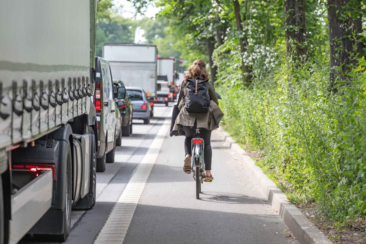 Eine Radfahrerin fährt zwischen stockendem Autoverkehr und grünem Straßenrand durch die Stadt.