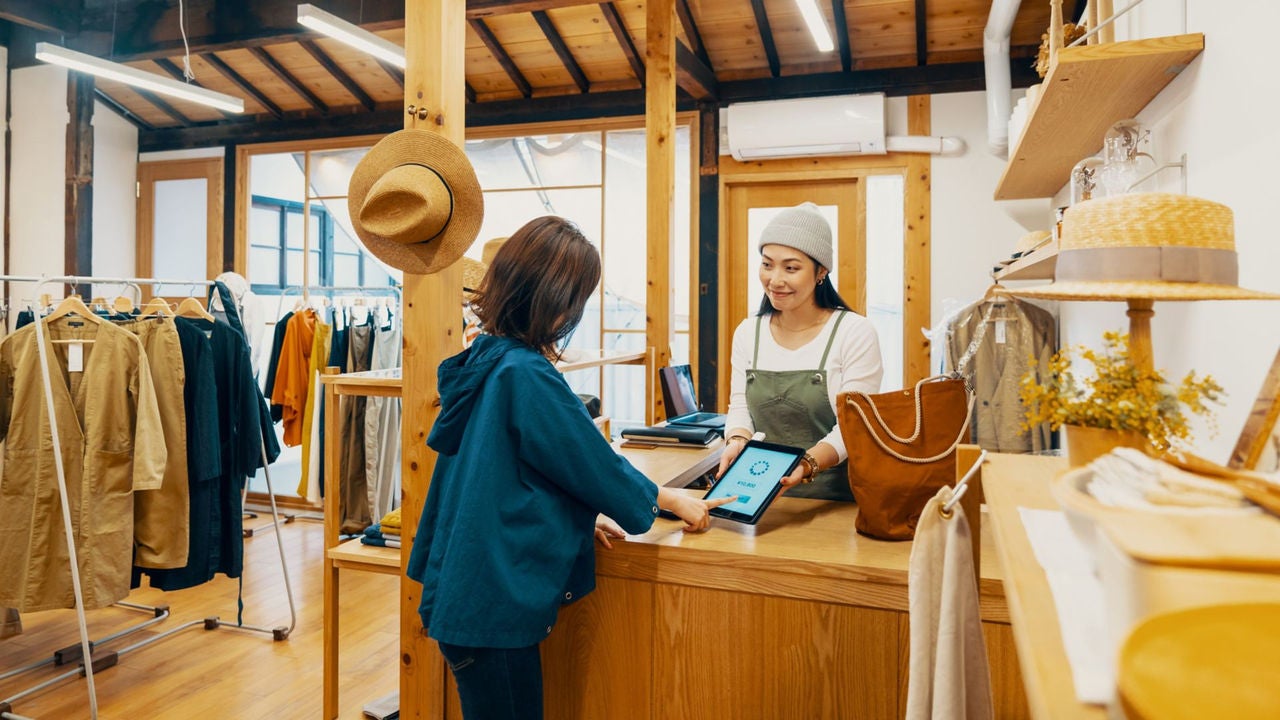 Female small business owner accepting mobile payment via digital tablet in a clothing store in Japan
