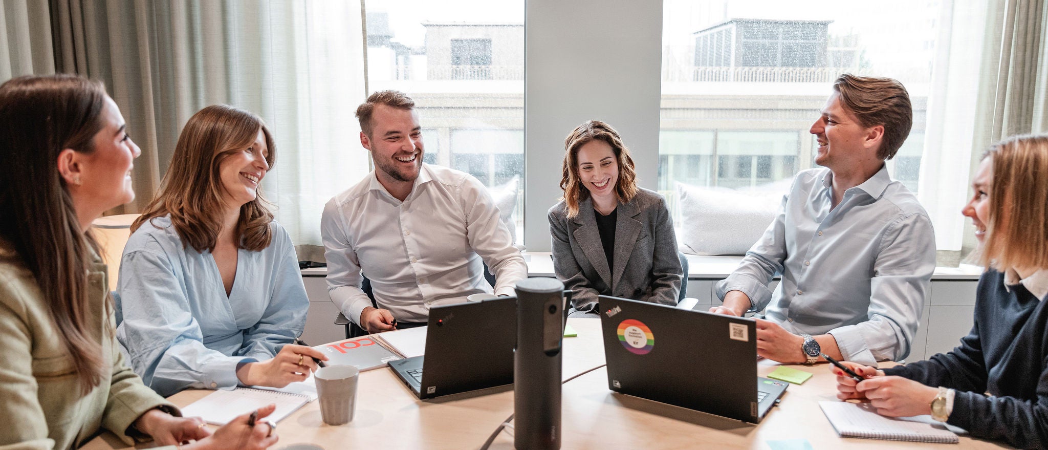 Grupp som arbetar vid konferensbord med bärbara datorer, anteckningar och material på bordet