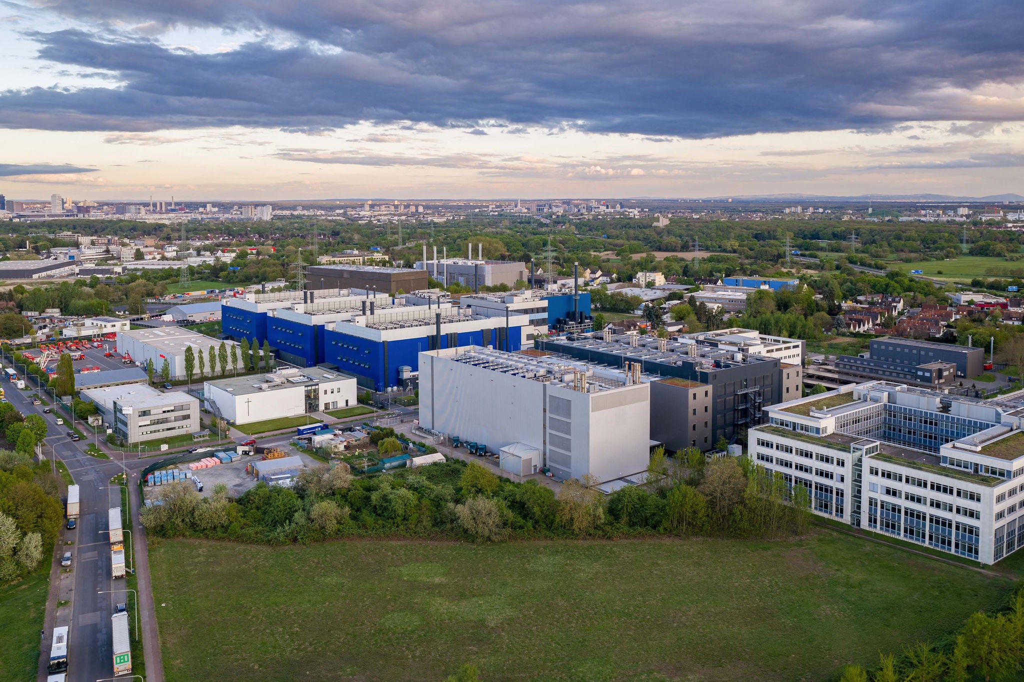 Luftaufnahme des Rechenzentrumskomplexes „Digital Realty Frankfurt FRA30“ mit modernen Industriegebaeuden und Gruenflaechen unter bewoelktem Himmel in Frankfurt am Main, Hessen, Deutschland.