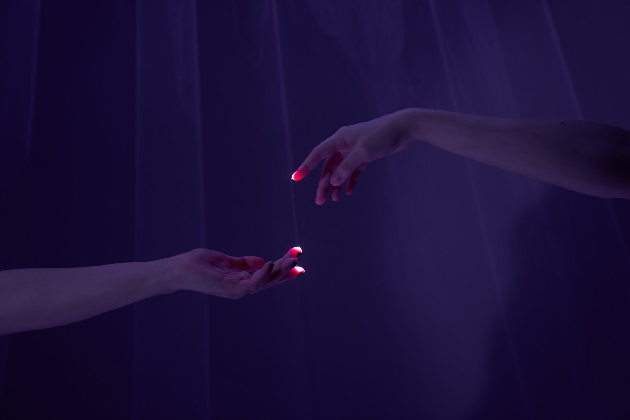 Two hands of different people reach out to each other through the laser beams on a purple background.  The concept of helping hand with copy space.