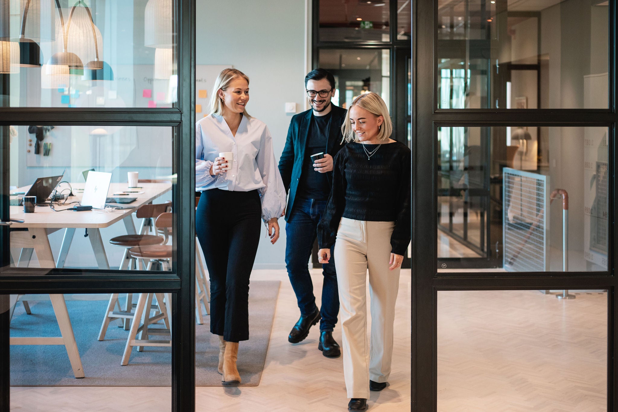Yrkesverksamma som promenerar och diskuterar arbete i en modern kontorskorridor.