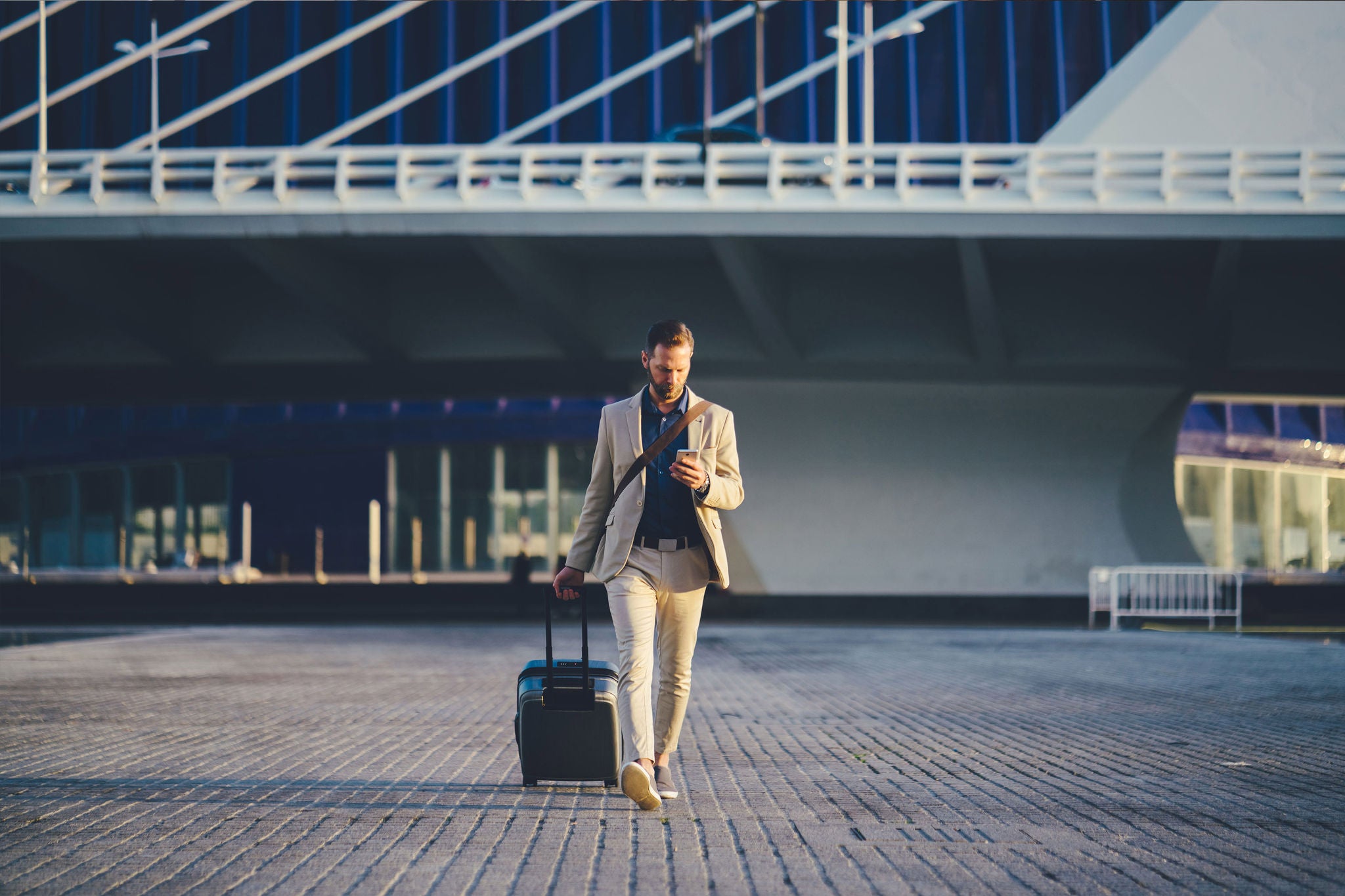 Young businessman with suitcase just arriving in Valencia and texting on phone