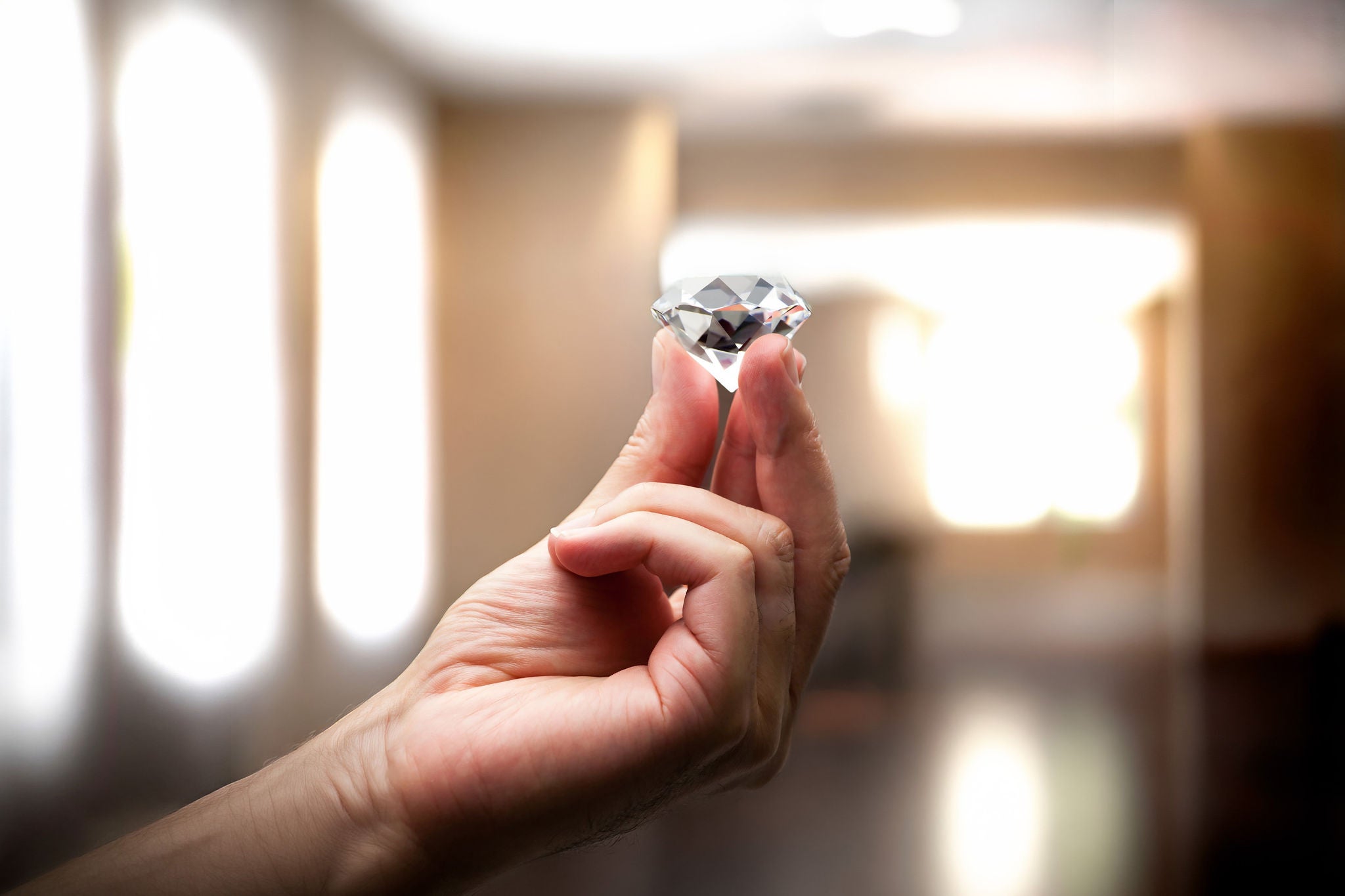 Eine Hand hält einen funkelnden Diamanten vor einem hellen, unscharfen Hintergrund.
