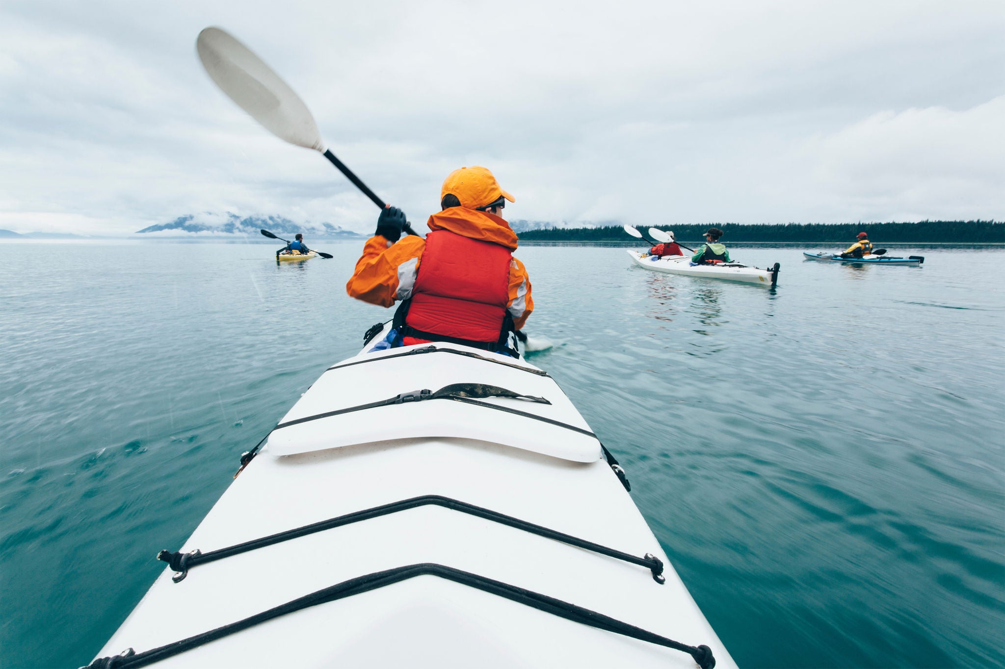 A person paddling in a double sea kayak on calm water off the coast of Alaska