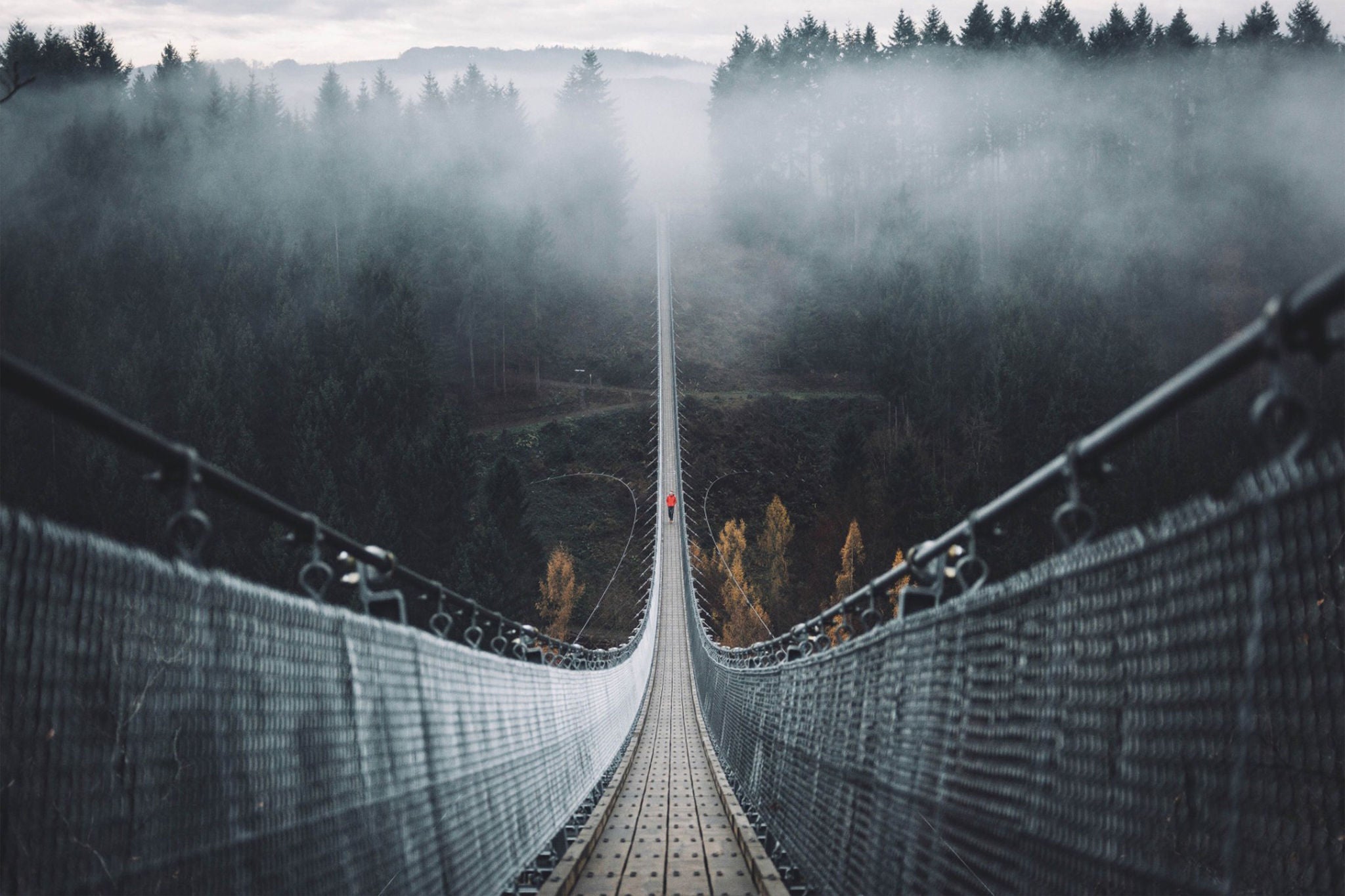 Man walking over suspension bridge in the fog