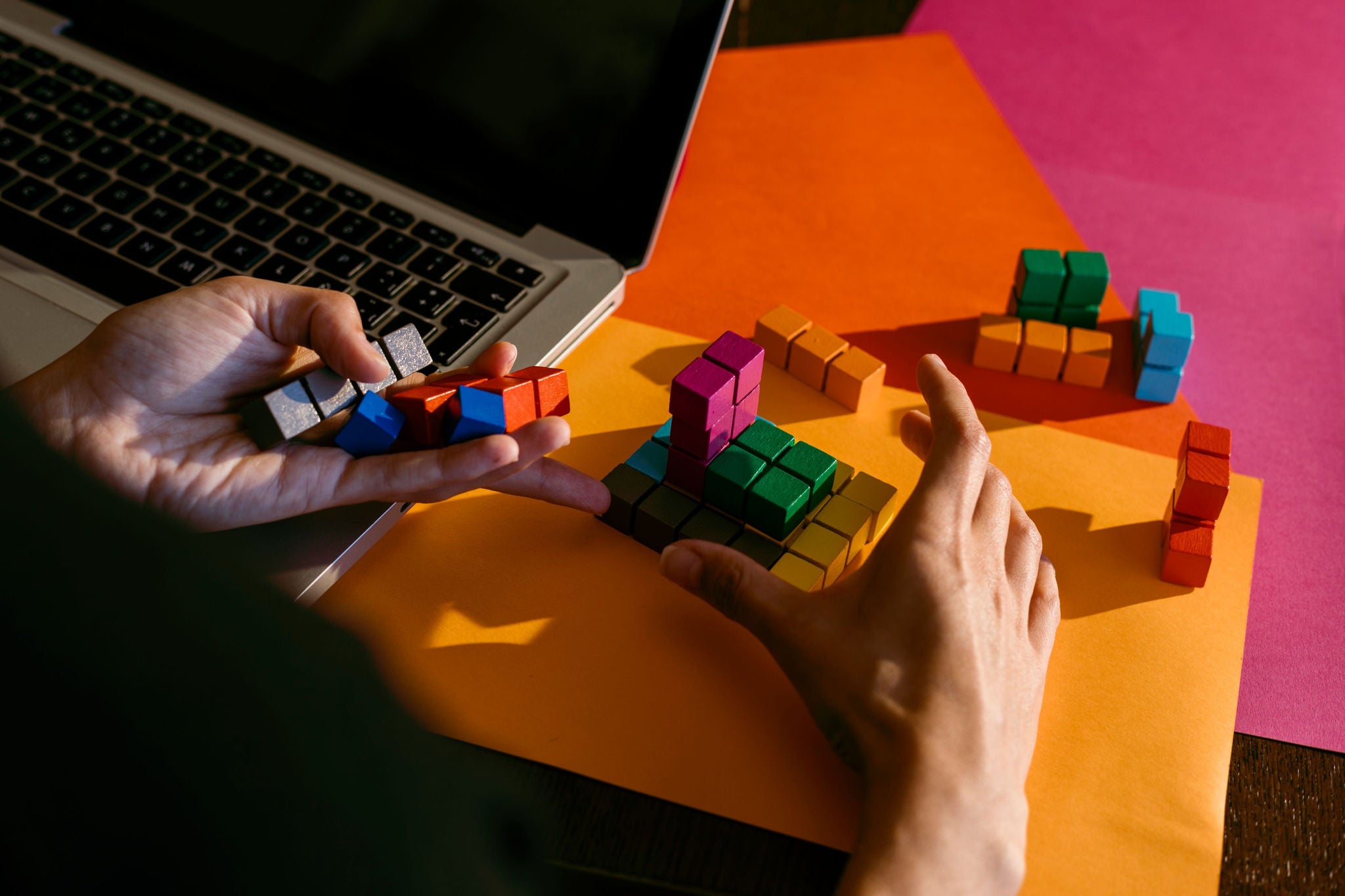 Hands solving colorful puzzle blocks near laptop
