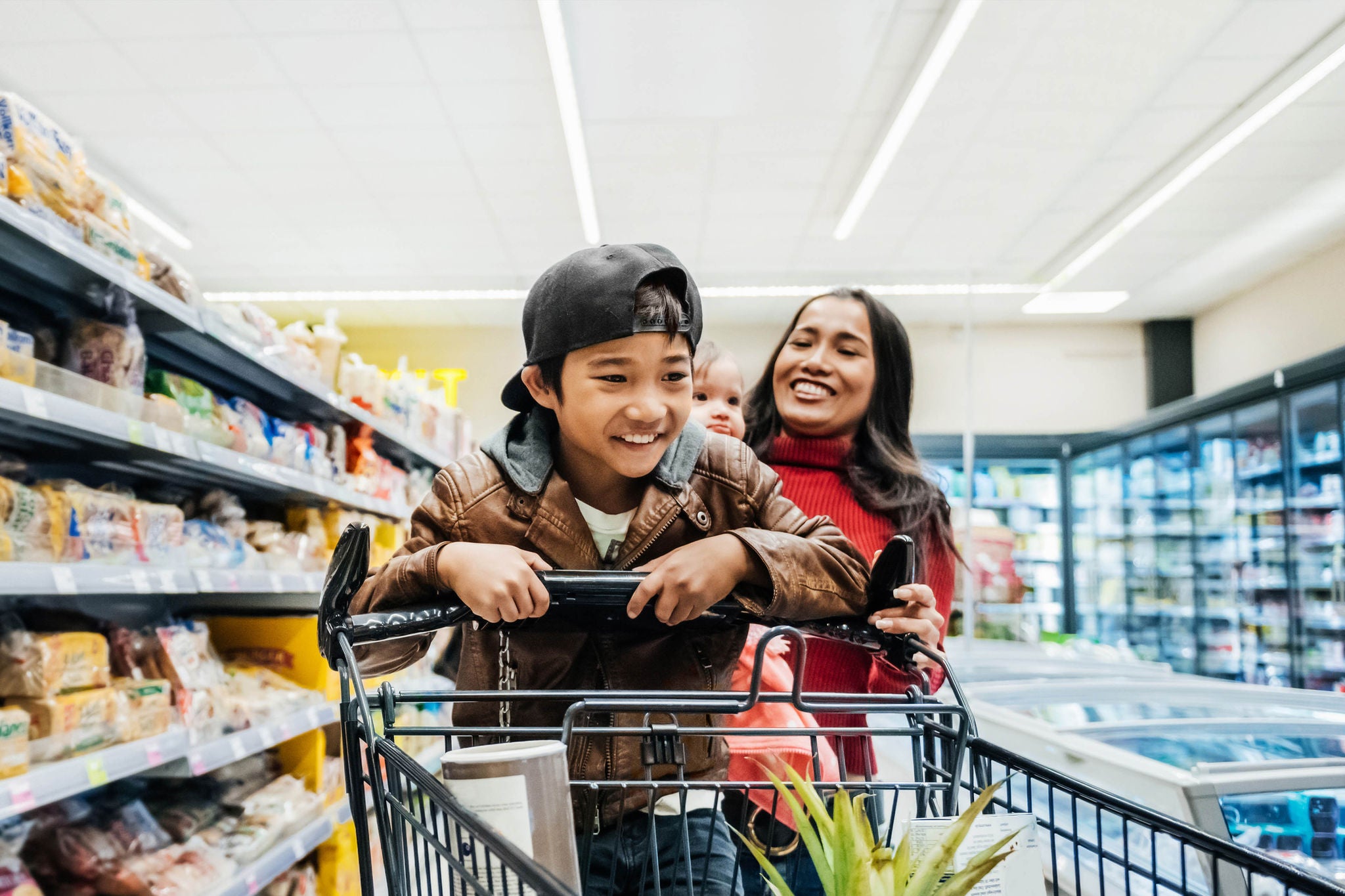 A young boy having fun on a shopping cart while out buying groceries with his family.