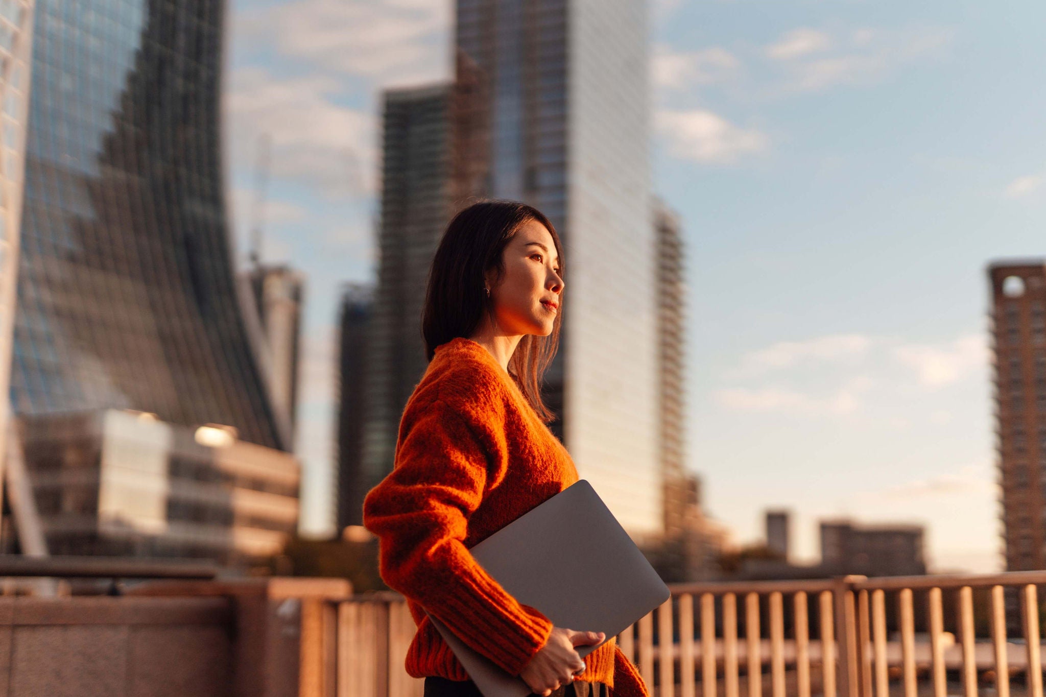 Woman holding a laptop on a city bridge