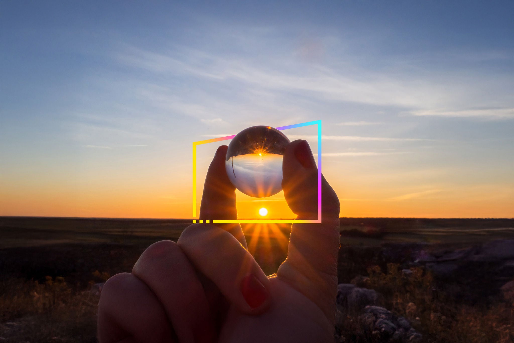 View of a sunset landscape reflected in a crystal ball in the hand of an unrecognizable person and sunbeams beside