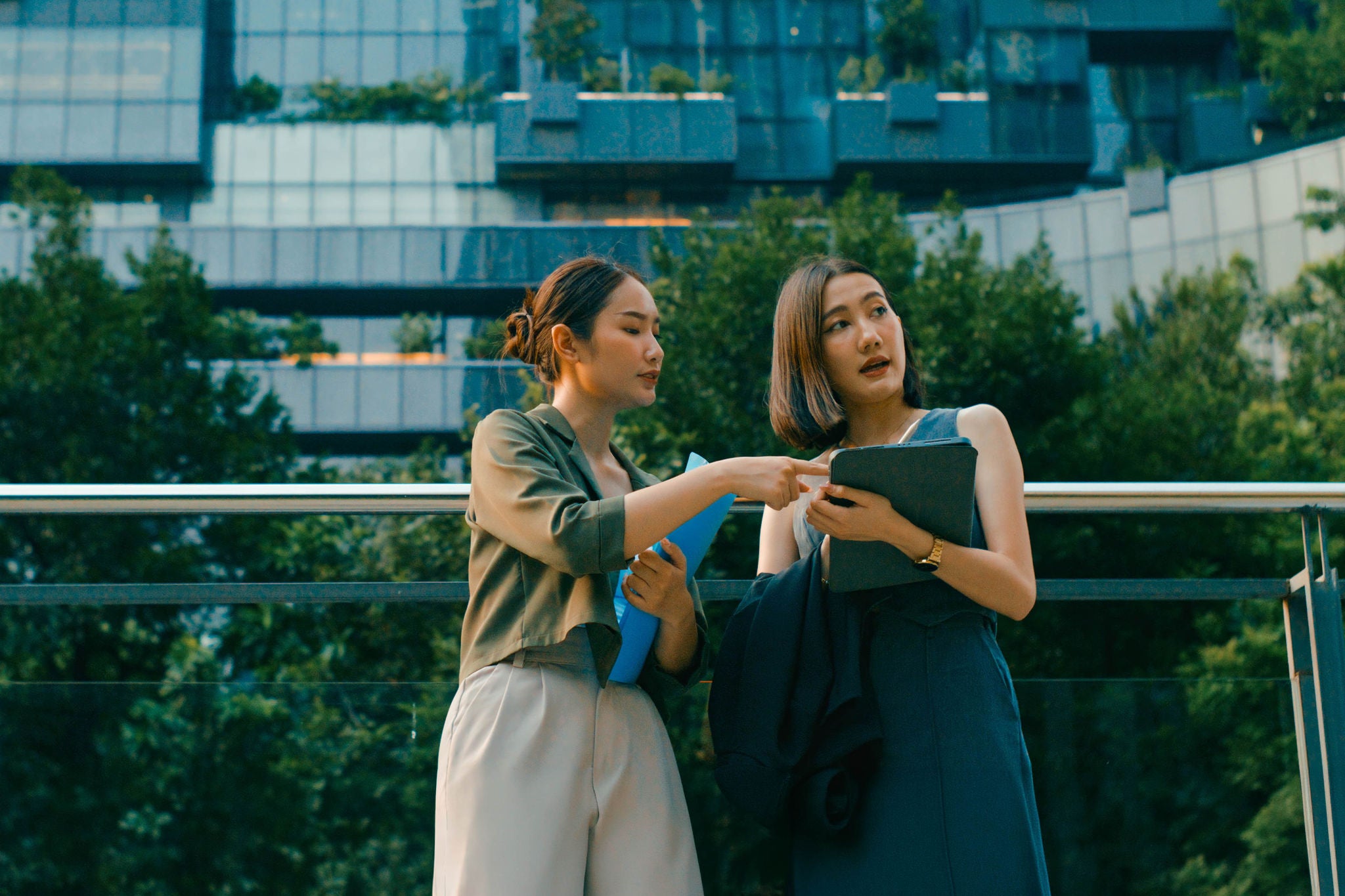 Two young Asian businesswomen meeting business strategy discussion talk outside modern office building