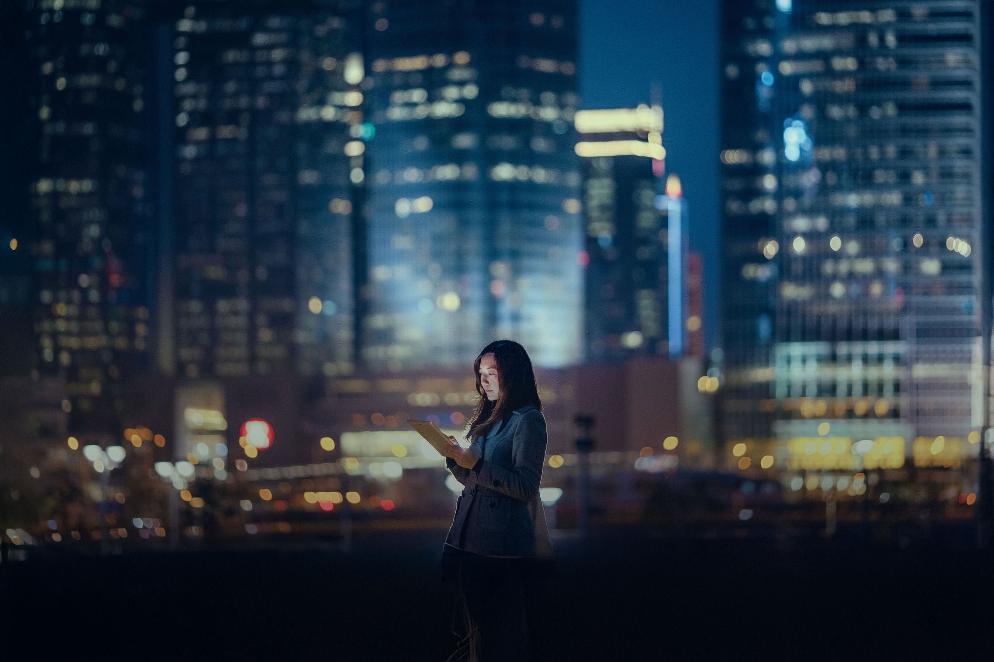 Photo of a woman using a tablet at night with skyscrapers in the background