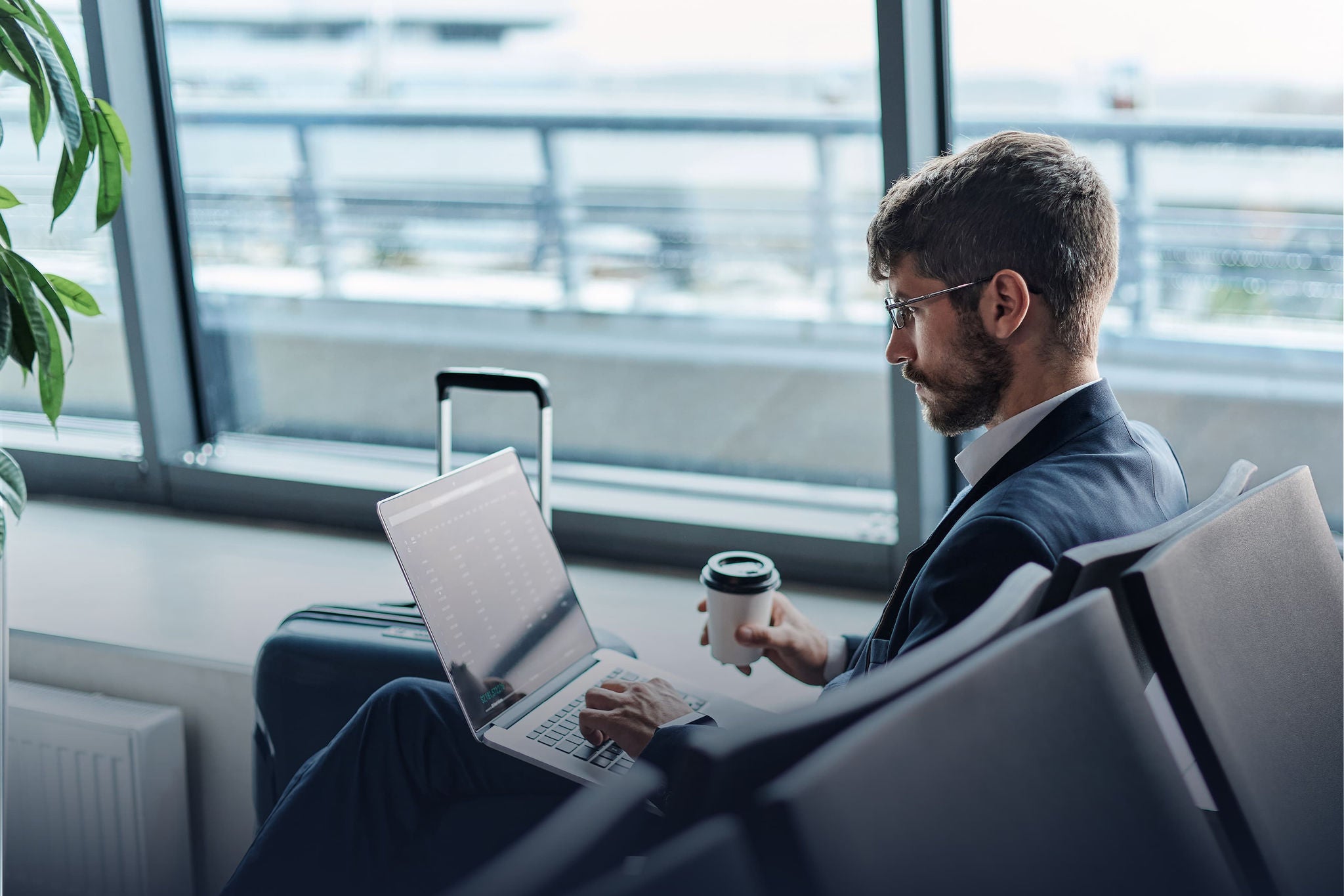 Business traveler working on a laptop while waiting at an airport terminal.