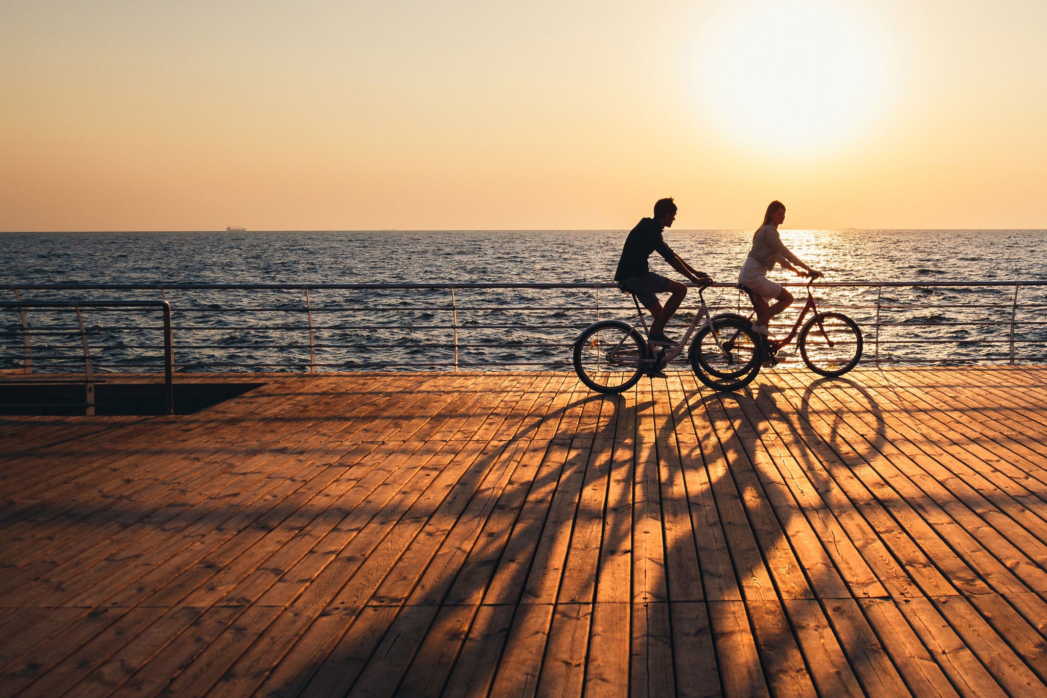 Two people cycling along a seaside boardwalk at sunset