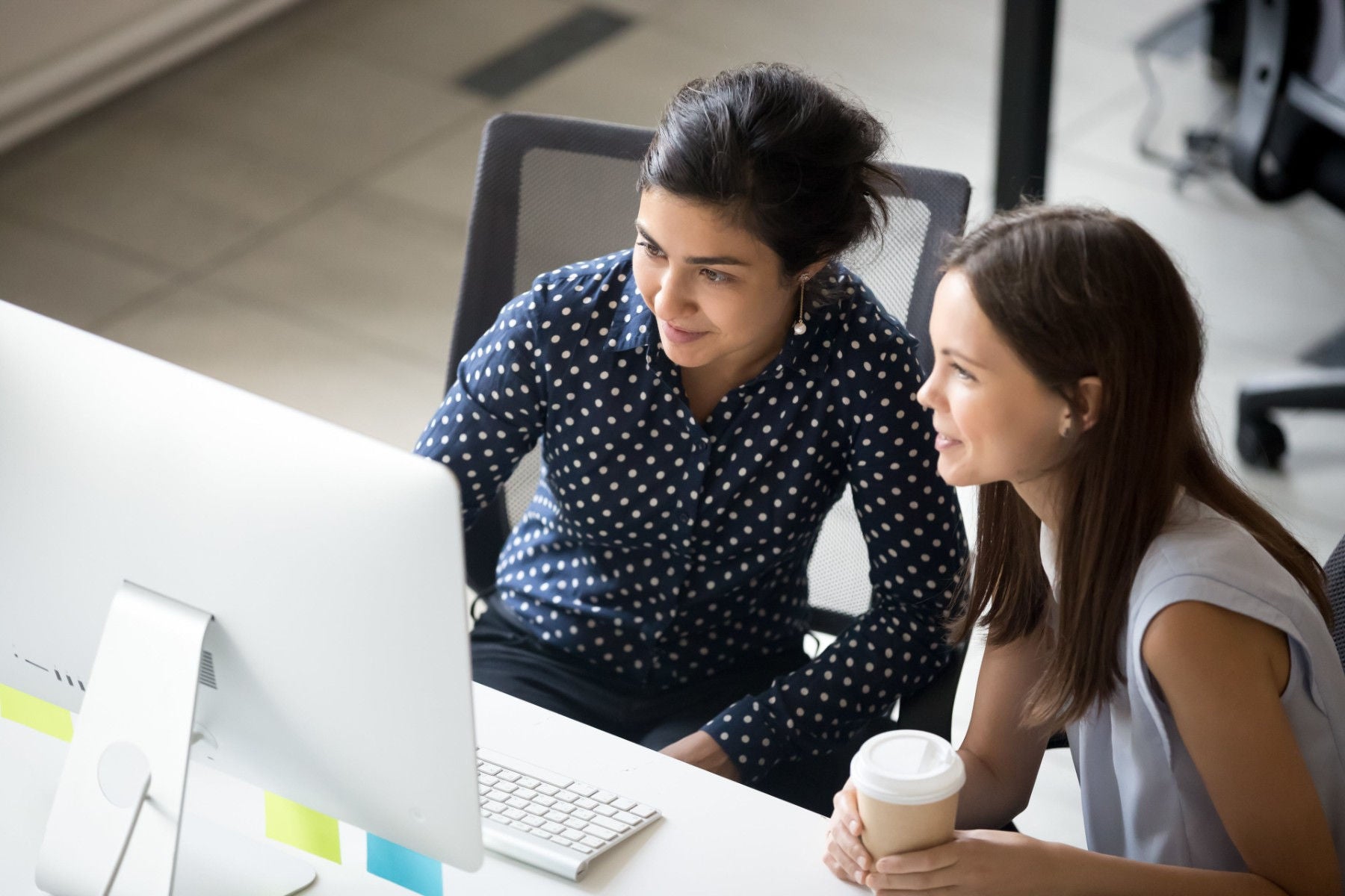 Dos mujeres sentadas observando la pantalla de una computadora de escritorio