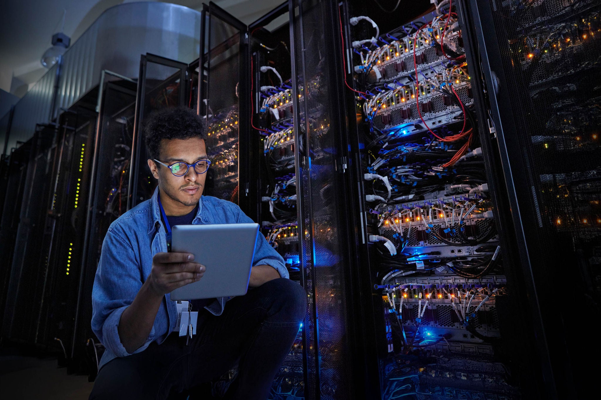 Focused male IT technician using digital tablet in dark server room
