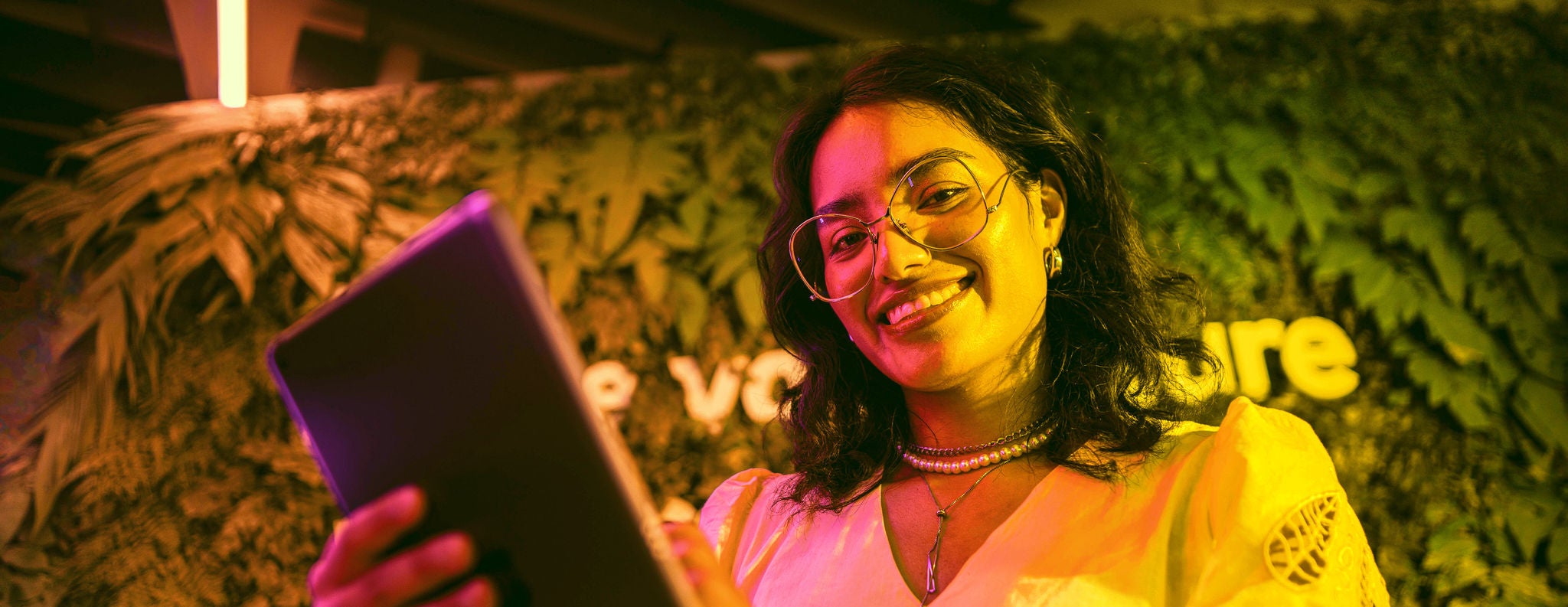 Mujer sonriente con lentes que mira a cámara con una tablet en la mano