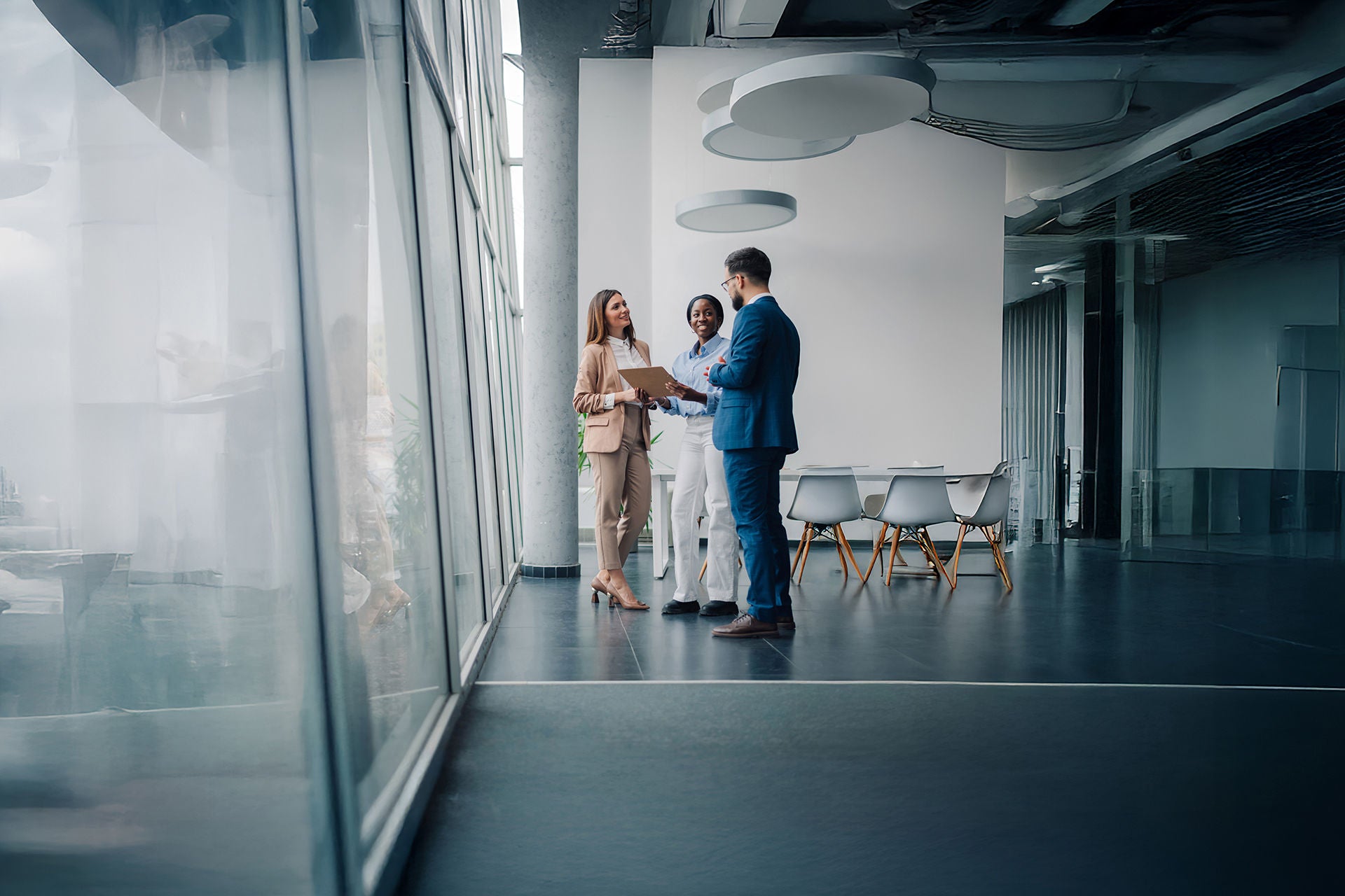 Multi-ethnic business team discussing in a modern office hallway with large windows and natural light