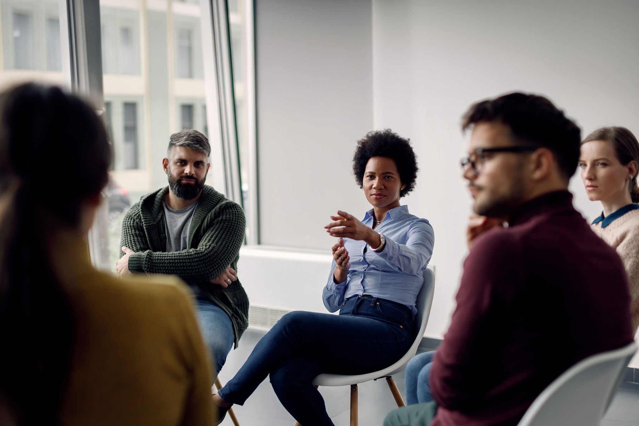African American therapist leading a group therapy and pointing at one of the participants.