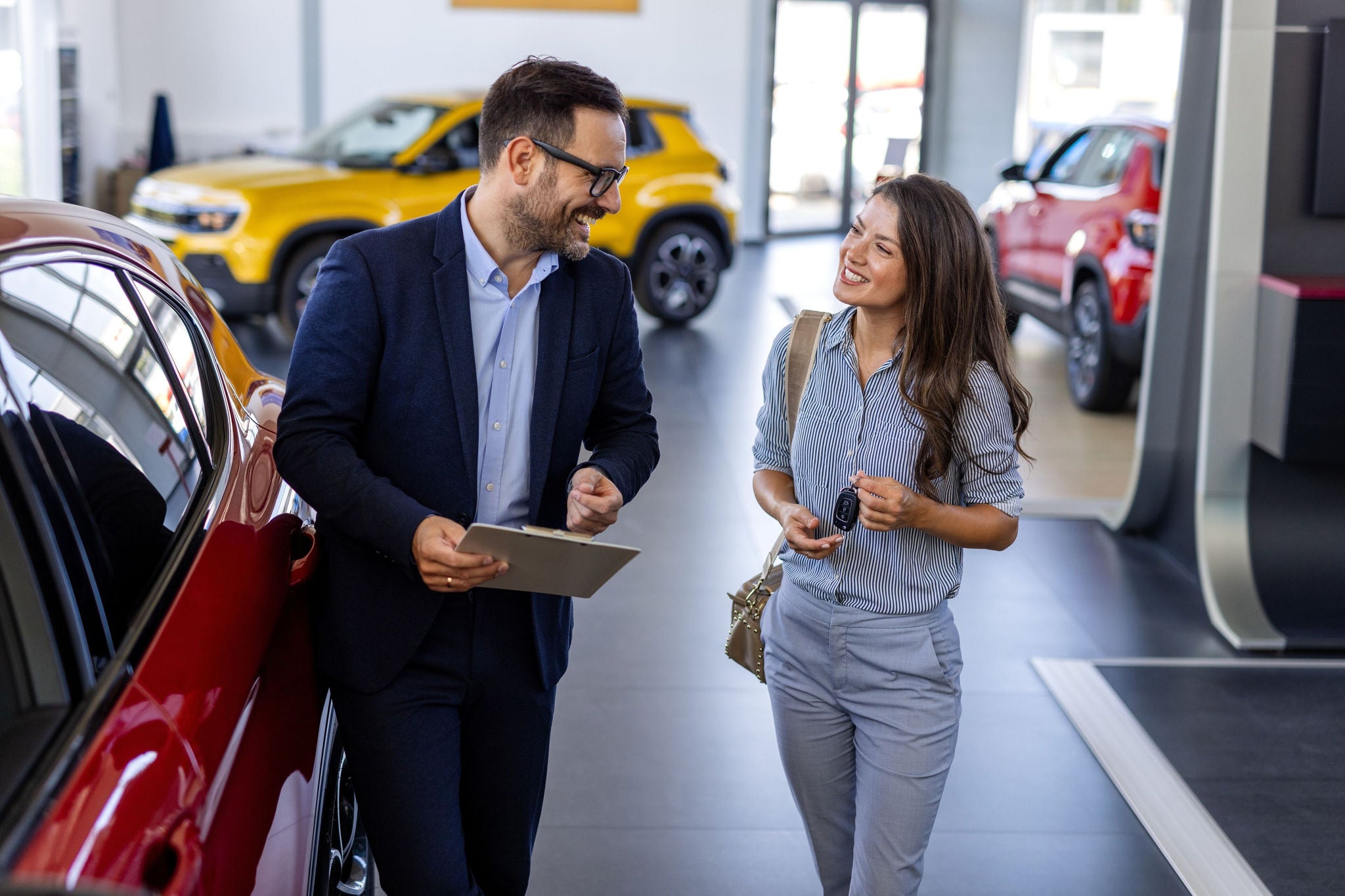 Beautiful young woman is talking to handsome car dealership worker while choosing a car in dealership