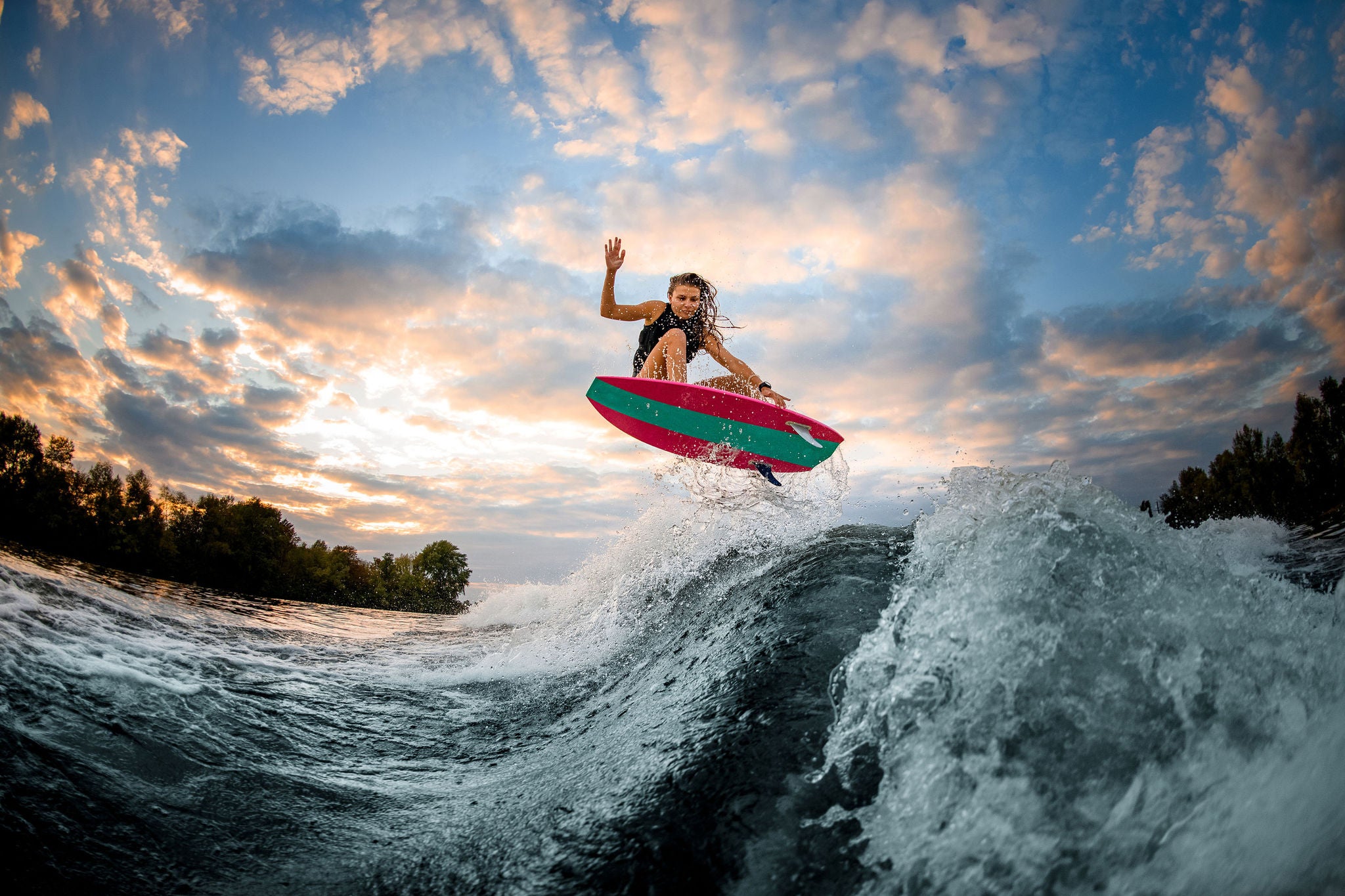 Woman jumping over big splashing wave on surf style wakeboard.