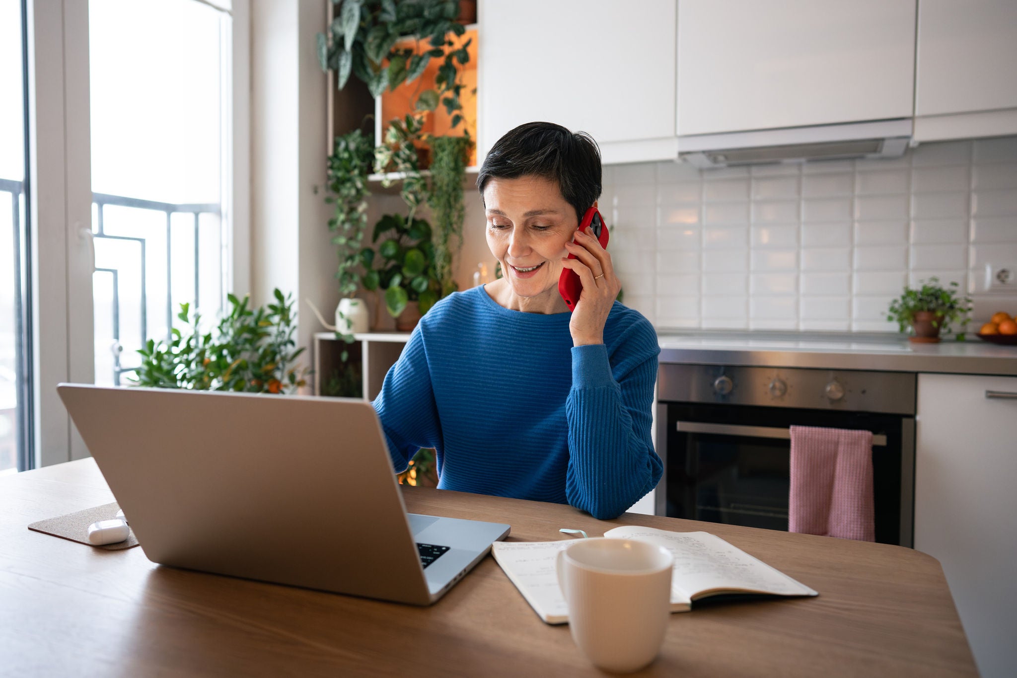Selbstbewusste, reife Frau, die laechelt, waehrend sie zu Hause mit ihrem Smartphone telefoniert 
