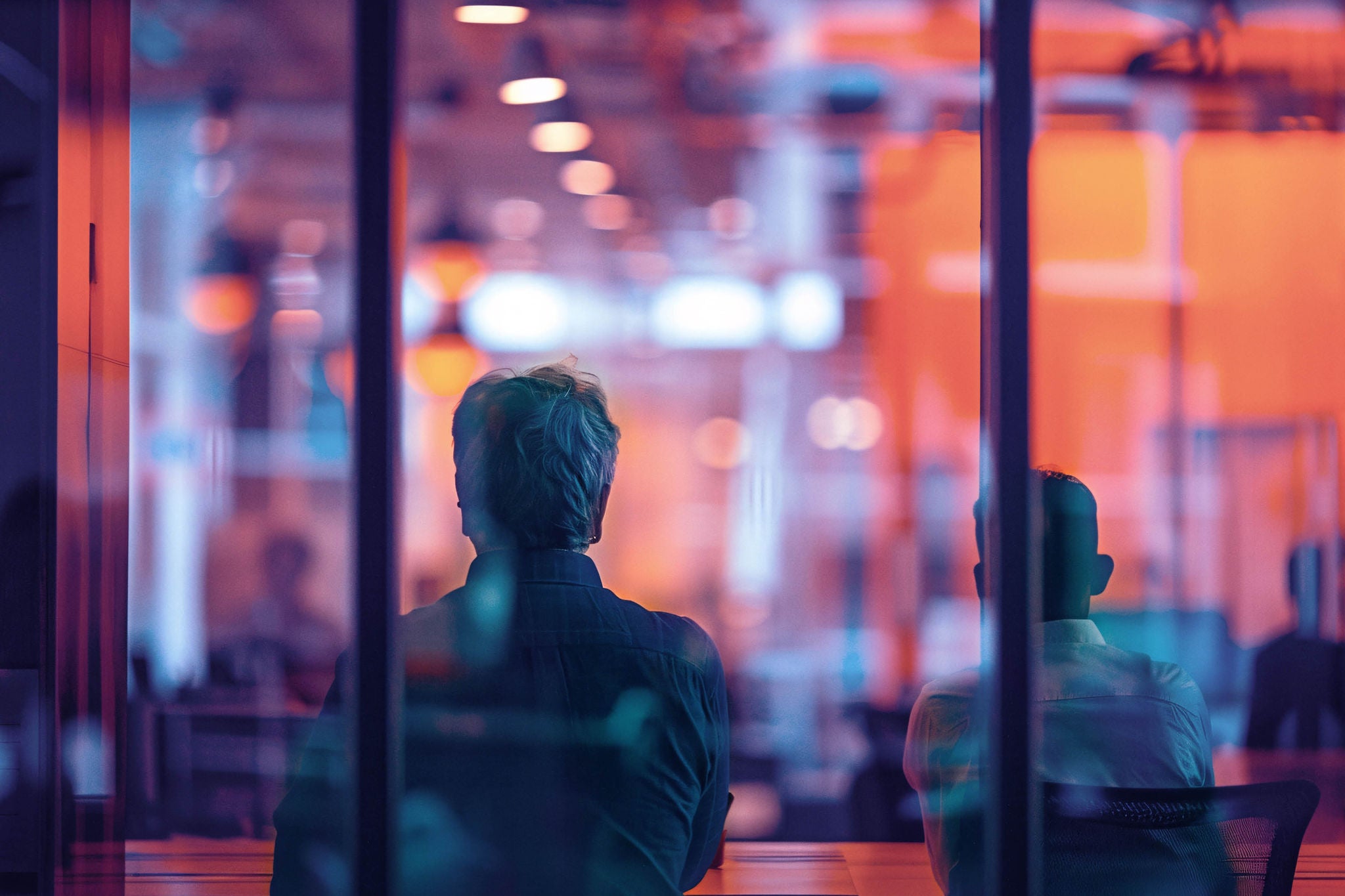 Two people seated in a glass office with warm lighting