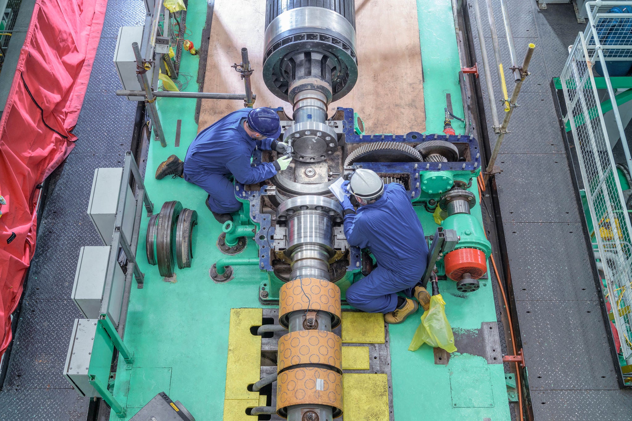 Overhead view of engineers inspecting gears on generator in turbine hall of nuclear power station