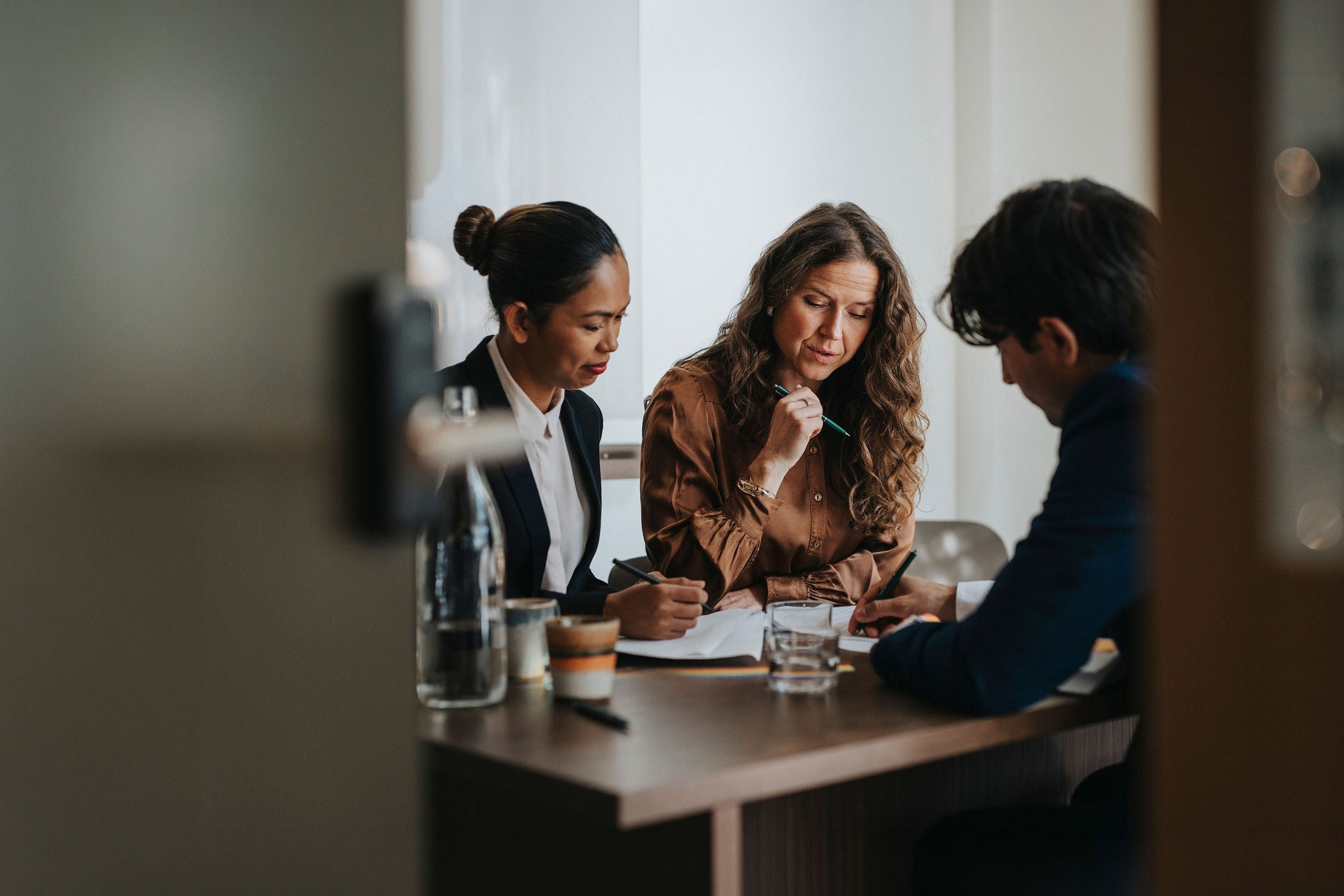 Young businessman writing while discussing strategy with female colleagues sitting at desk in office