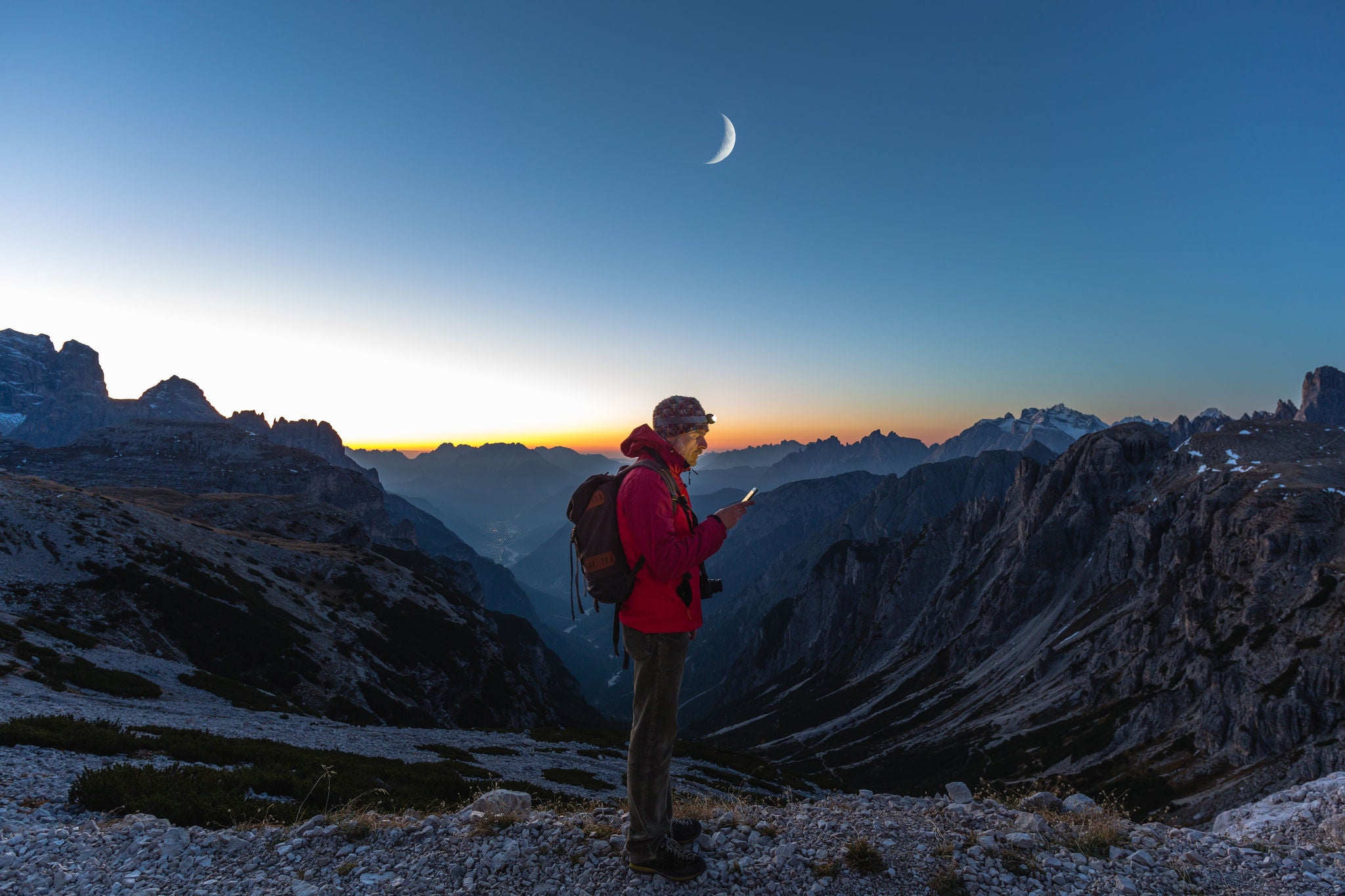 Hiker looking at map on mobile device in mountains at sunset.
