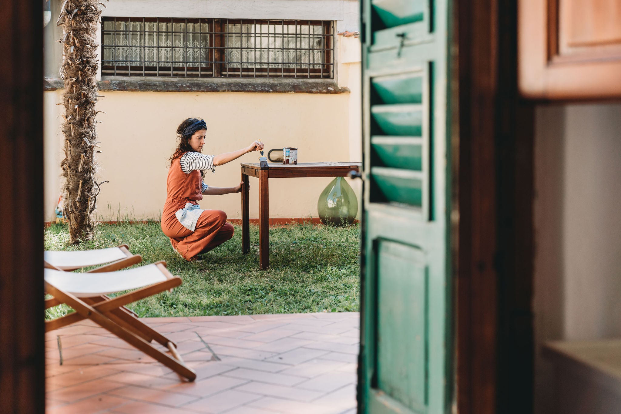 Young woman painting a wooden table in the back yard of her home. She's doing improvements during the Coronavirus Covid-19 quarantine.
